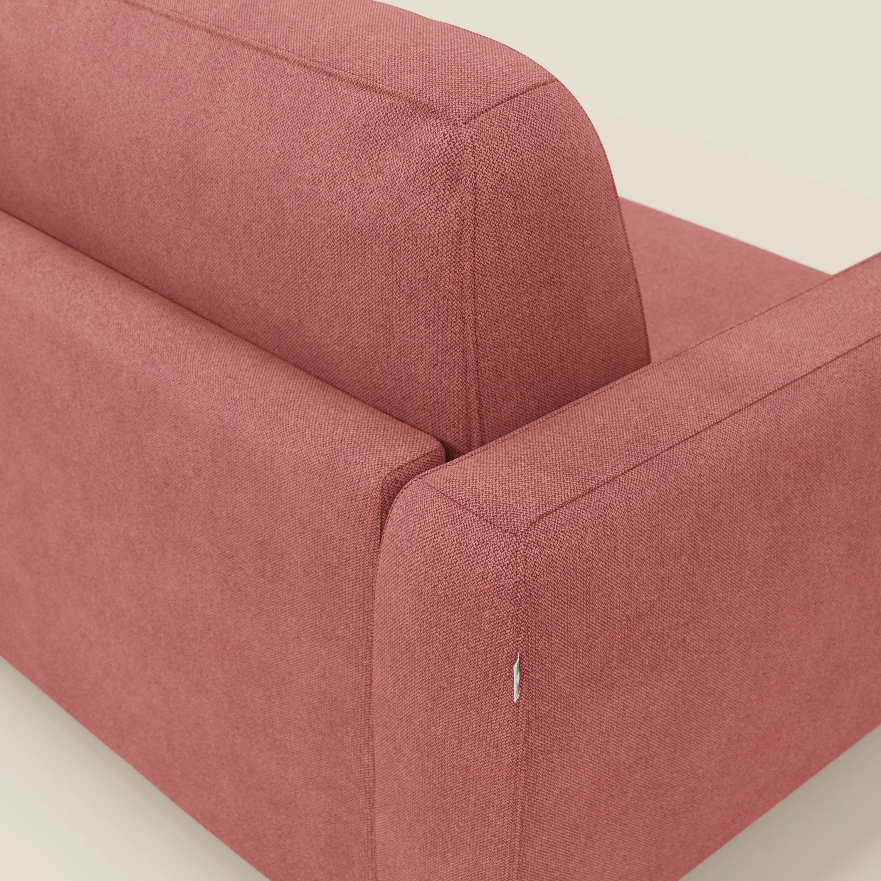 Primo piano del divano letto Leonida di Divani.Store in tessuto smacchiabile T23 rosso ciliegia, che mostra lo schienale e il bracciolo con cuciture dettagliate, l'imbottitura strutturata e una piccola etichetta bianca. Lo sfondo è una superficie liscia di colore beige chiaro.