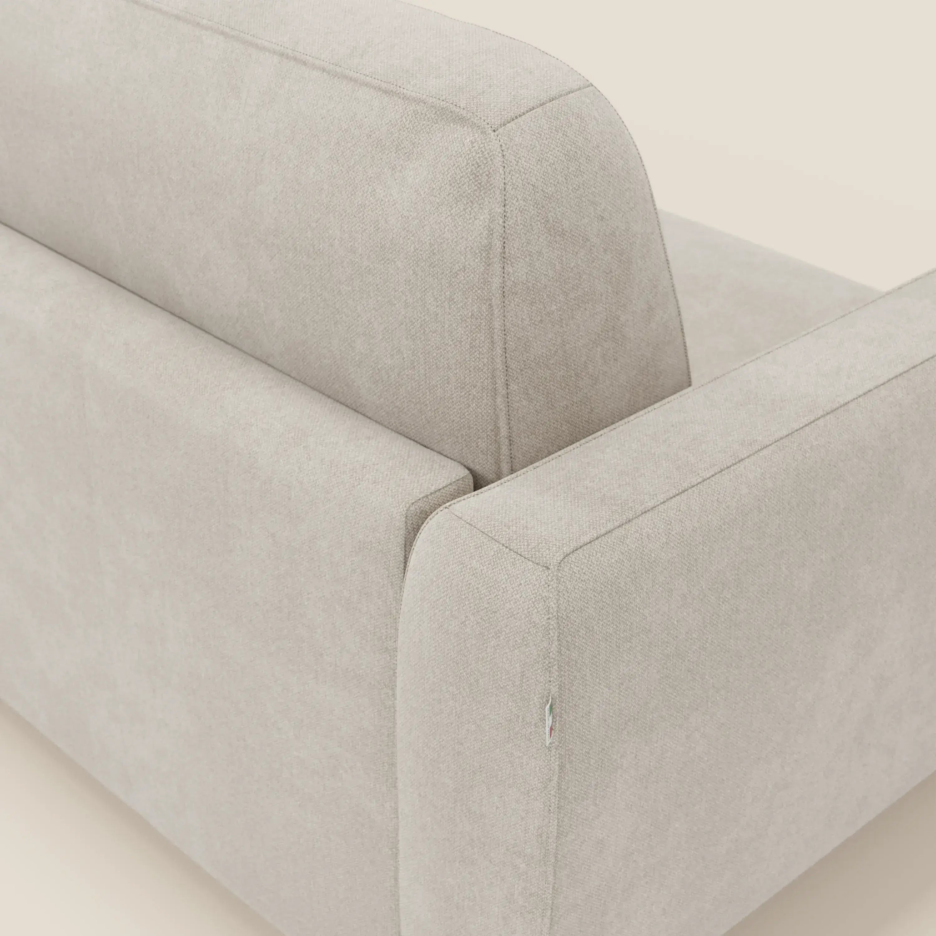 Un primo piano angolato del divano letto sfoderabile Leonida di Divani.Store in tessuto Smacchiabile T23 panna mostra il bracciolo, lo schienale e la seduta. Il tessuto morbido e strutturato e lo sfondo neutro ne evidenziano il design minimalista e moderno.