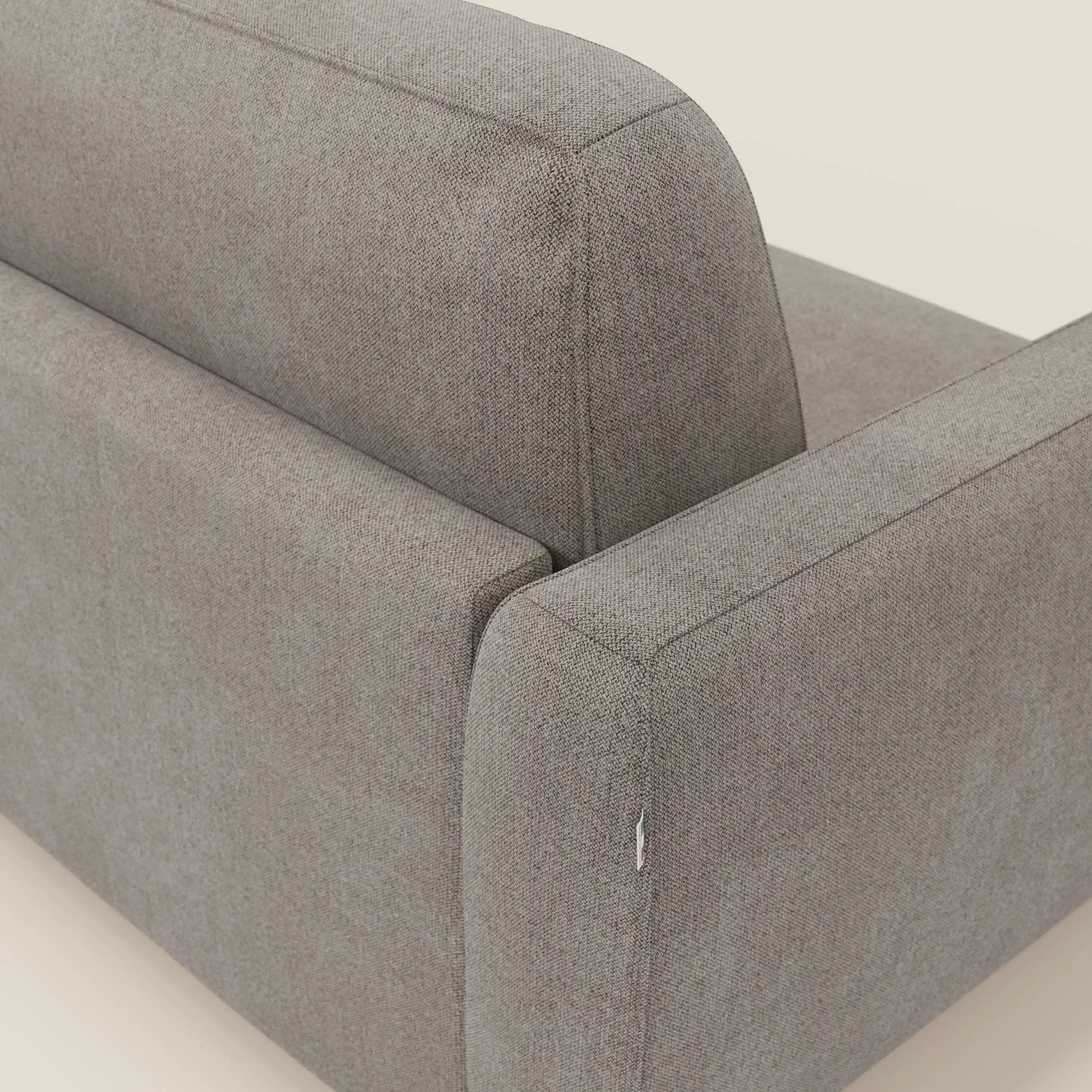 Primo piano dello schienale e del bracciolo del divano letto sfoderabile Leonida di Divani.Store, rivestito in tessuto talpa Smacchiabile T23 con cuciture a vista e una piccola etichetta sul bracciolo. Lo sfondo è una superficie liscia di colore bianco sporco.