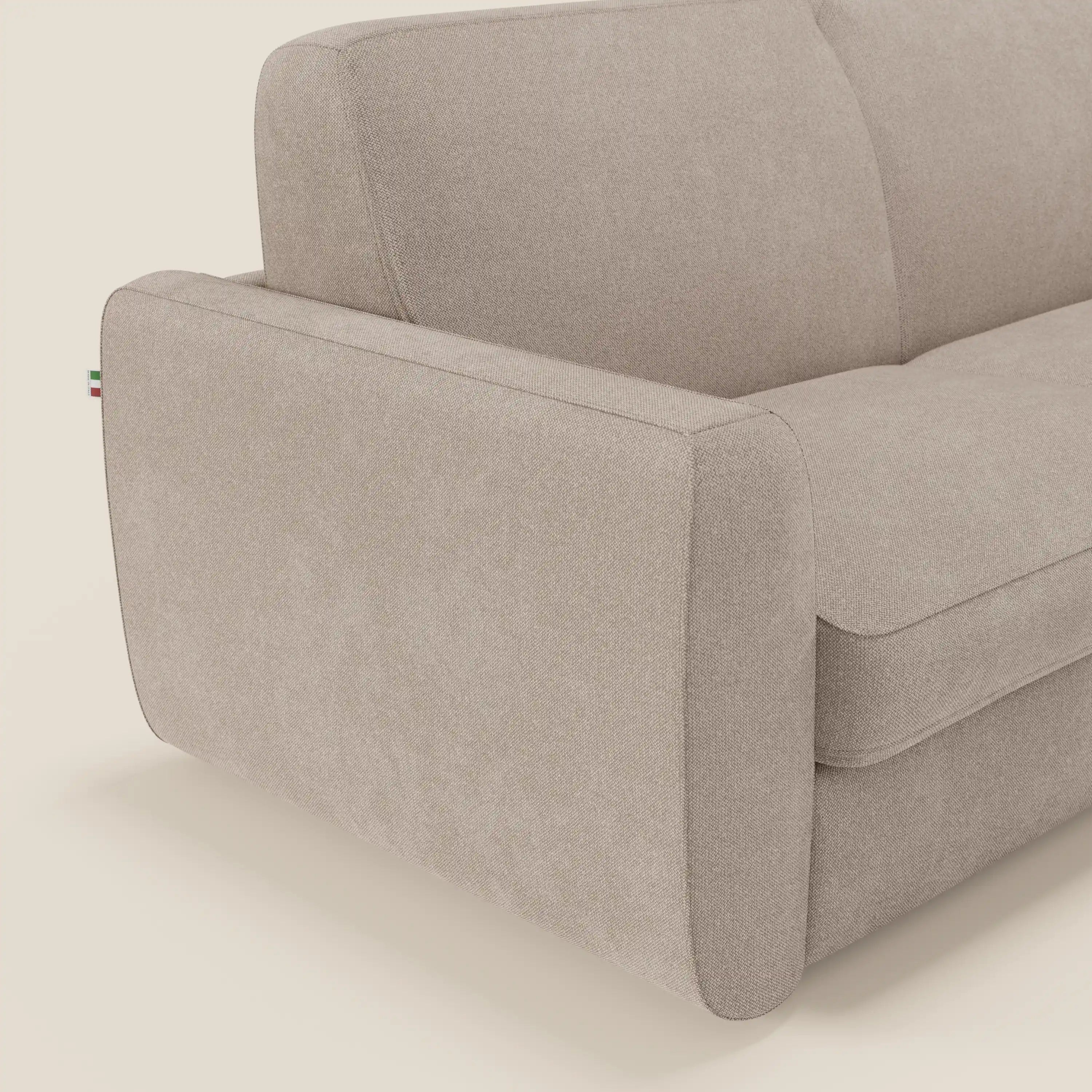 Un primo piano del divano letto sfoderabile Leonida di Divani.Store in smacchiabile T23 tortora mostra linee pulite, cuscini morbidi e un bracciolo sinistro spesso e arrotondato con una targhetta della bandiera italiana cucita nella cucitura.