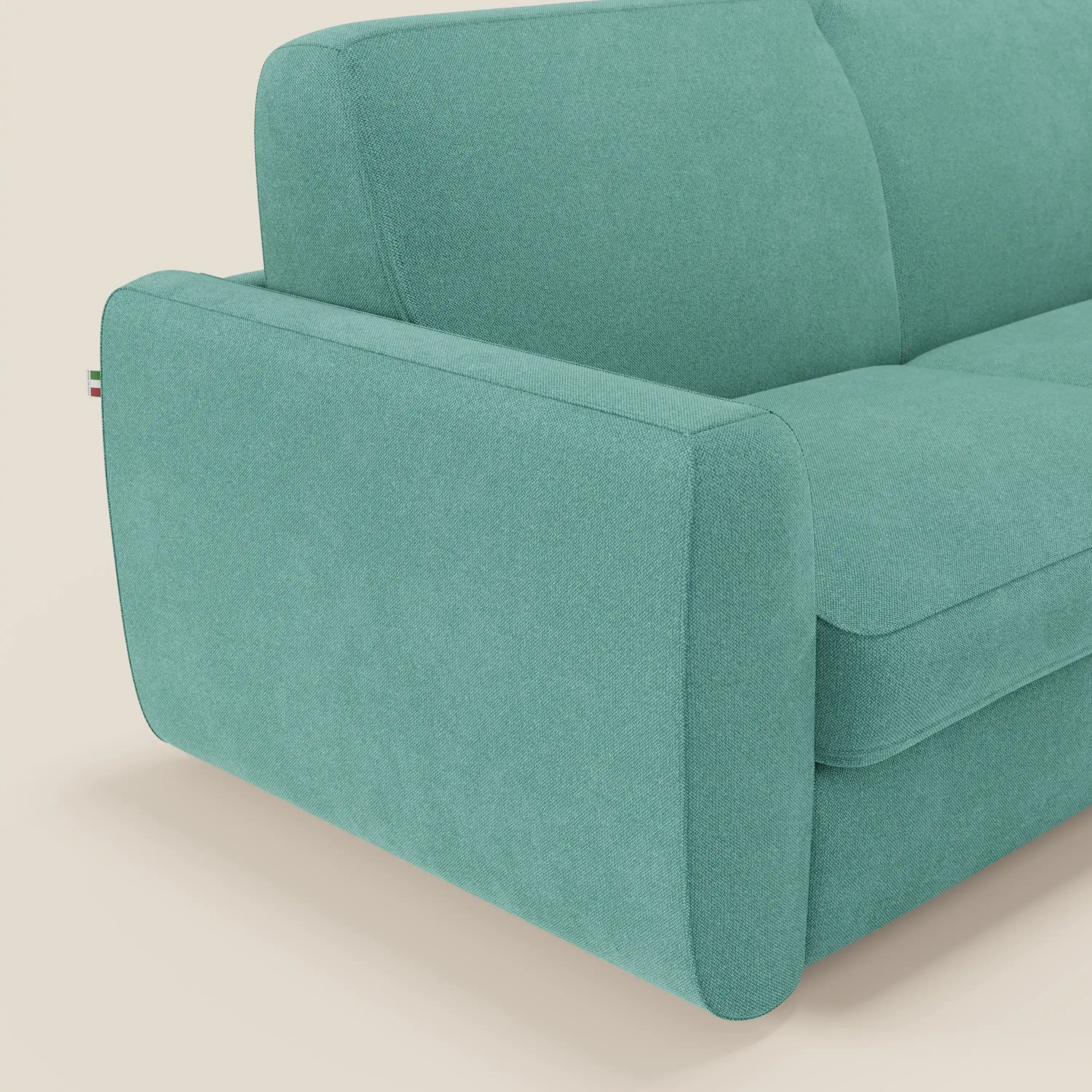 Un primo piano del divano letto sfoderabile Leonida di Divani.Store in tessuto antimacchia T23 verde acqua mette in evidenza il bracciolo arrotondato, la seduta e lo schienale con la targhetta della bandiera italiana. Il fondo beige chiaro ne esalta il look moderno.