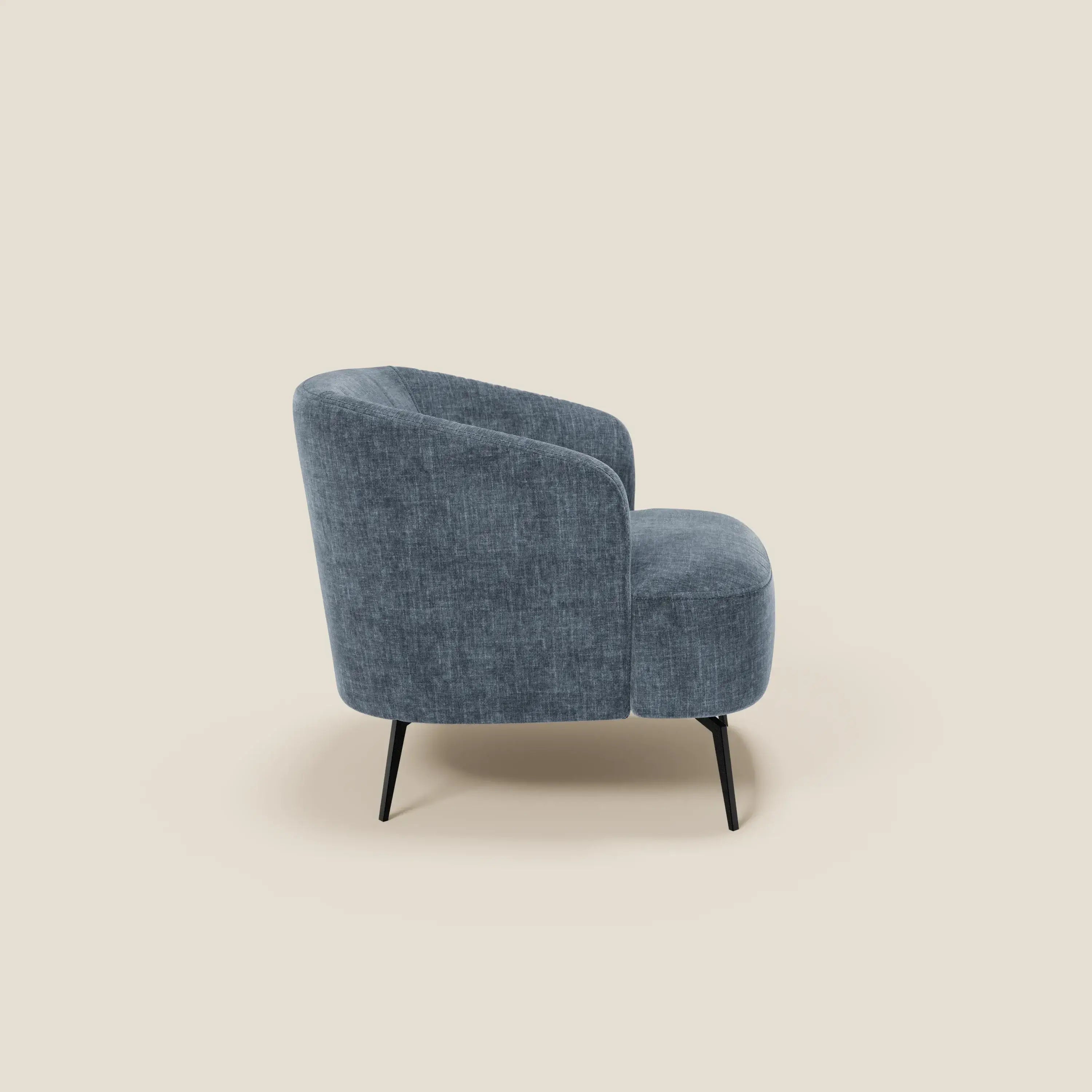 La poltroncina Renoa di Divani.Store, dal design moderno e con tessuto antimacchia ardesia blu T24, è presentata di profilo a sinistra. Presenta uno schienale e una seduta curvi con sottili gambe in metallo nero su sfondo beige chiaro.