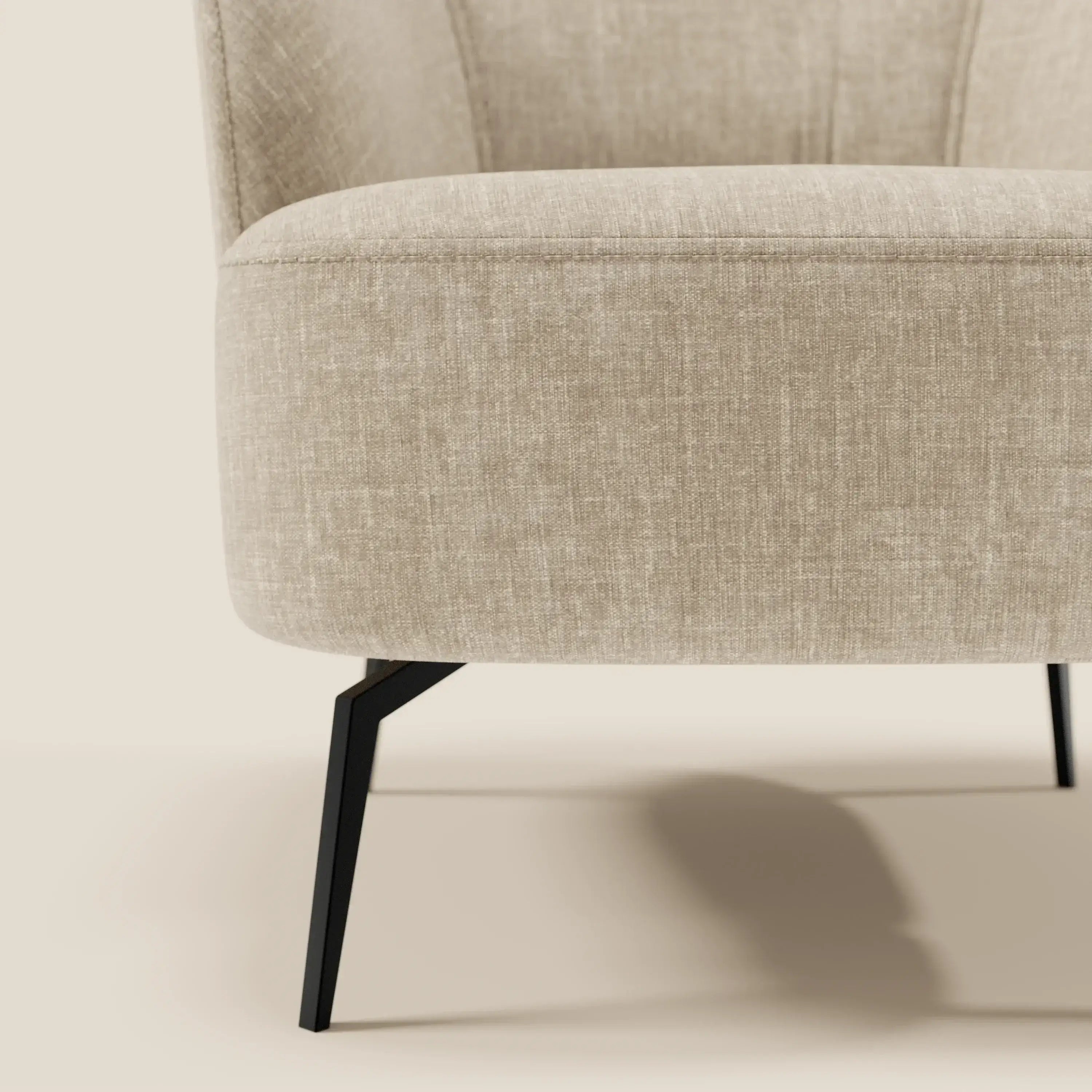 Primo piano della poltroncina Renoa di Divani.Store, con tessuto smacchiabile T24 beige e gambe in metallo nero. Lo schienale ricurvo e la morbida imbottitura sono una vetrina di moderna eleganza su uno sfondo chiaro e neutro.