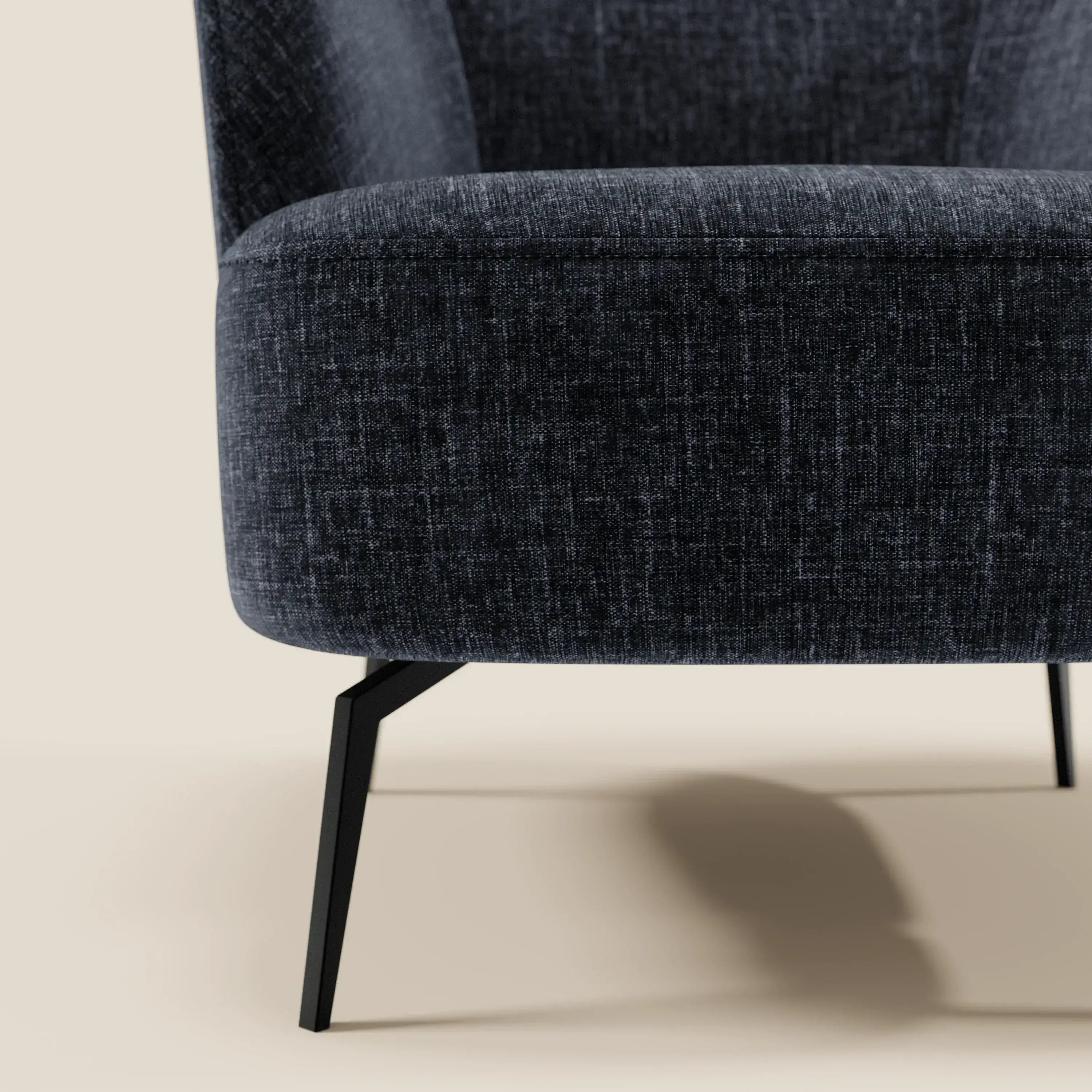 Primo piano della poltroncina Renoa di Divani.Store, caratterizzata da un'eleganza moderna grazie al tessuto smacchiabile T24 blu notte, alle gambe angolate in metallo nero e allo schienale alto e curvo, su uno sfondo beige chiaro. Design minimalista e contemporaneo.