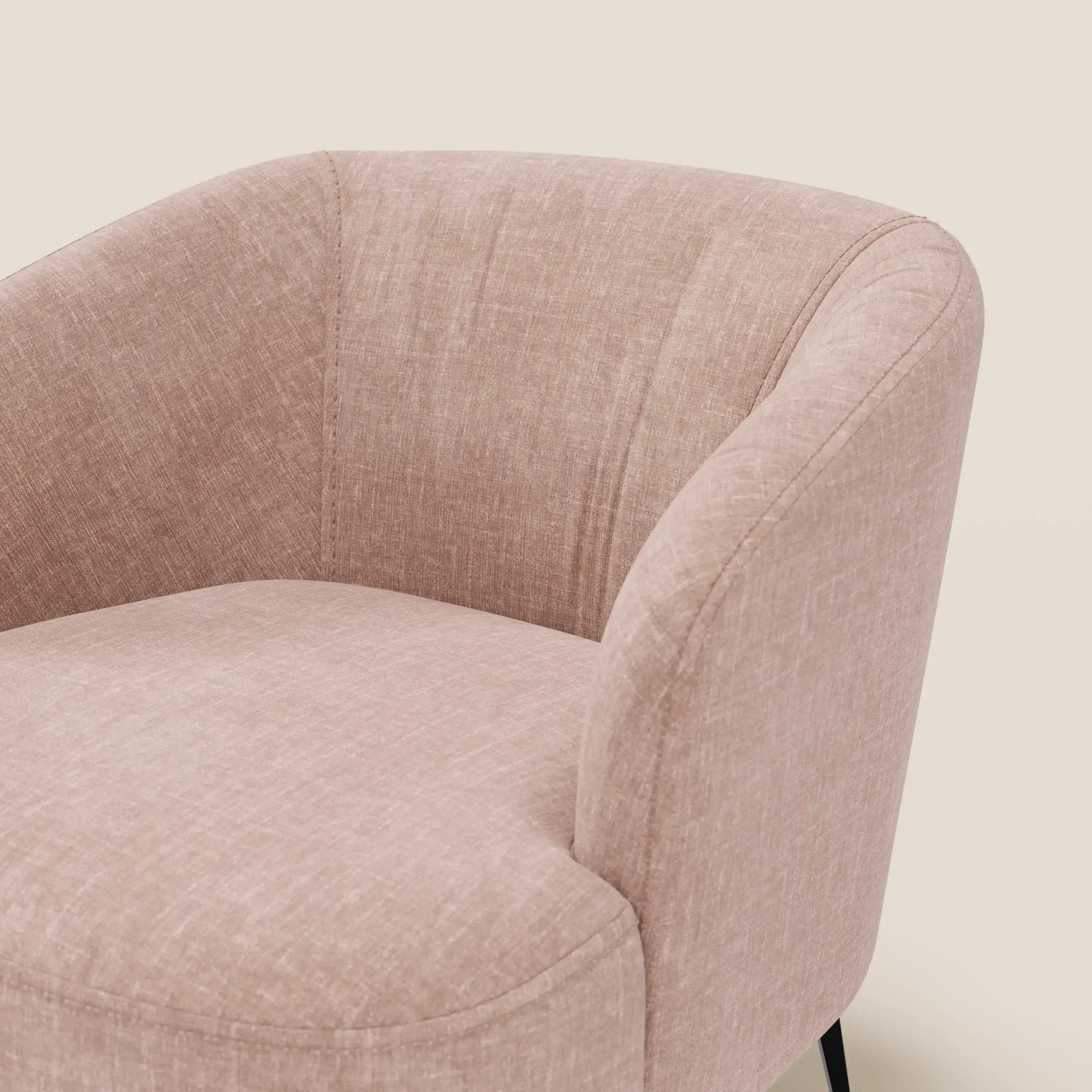 Primo piano della poltroncina Renoa di Divani.Store, caratterizzata da un'eleganza moderna in tessuto antimacchia T24 rosa cipria. Le curve morbide e la seduta imbottita poggiano su eleganti gambe in metallo nero, su uno sfondo beige.