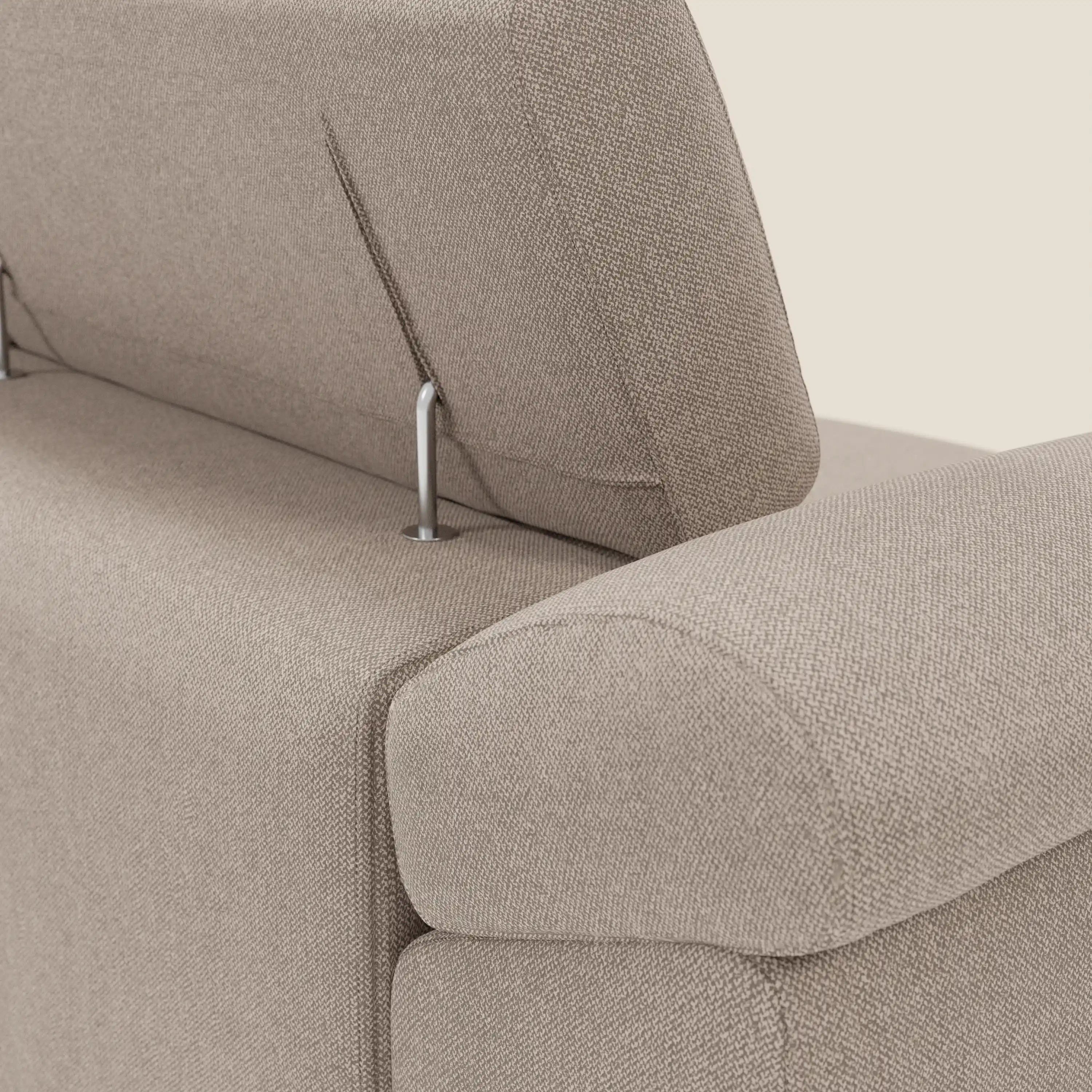 Primo piano del divano Donatello di Divani.Store in tessuto smacchiabile T23 tortora, con 3 sedute allungabili, braccioli contenitore e poggiatesta reclinabili con supporti in metallo. La trama intrecciata e i braccioli in tessuto aggiungono eleganza a uno sfondo chiaro.