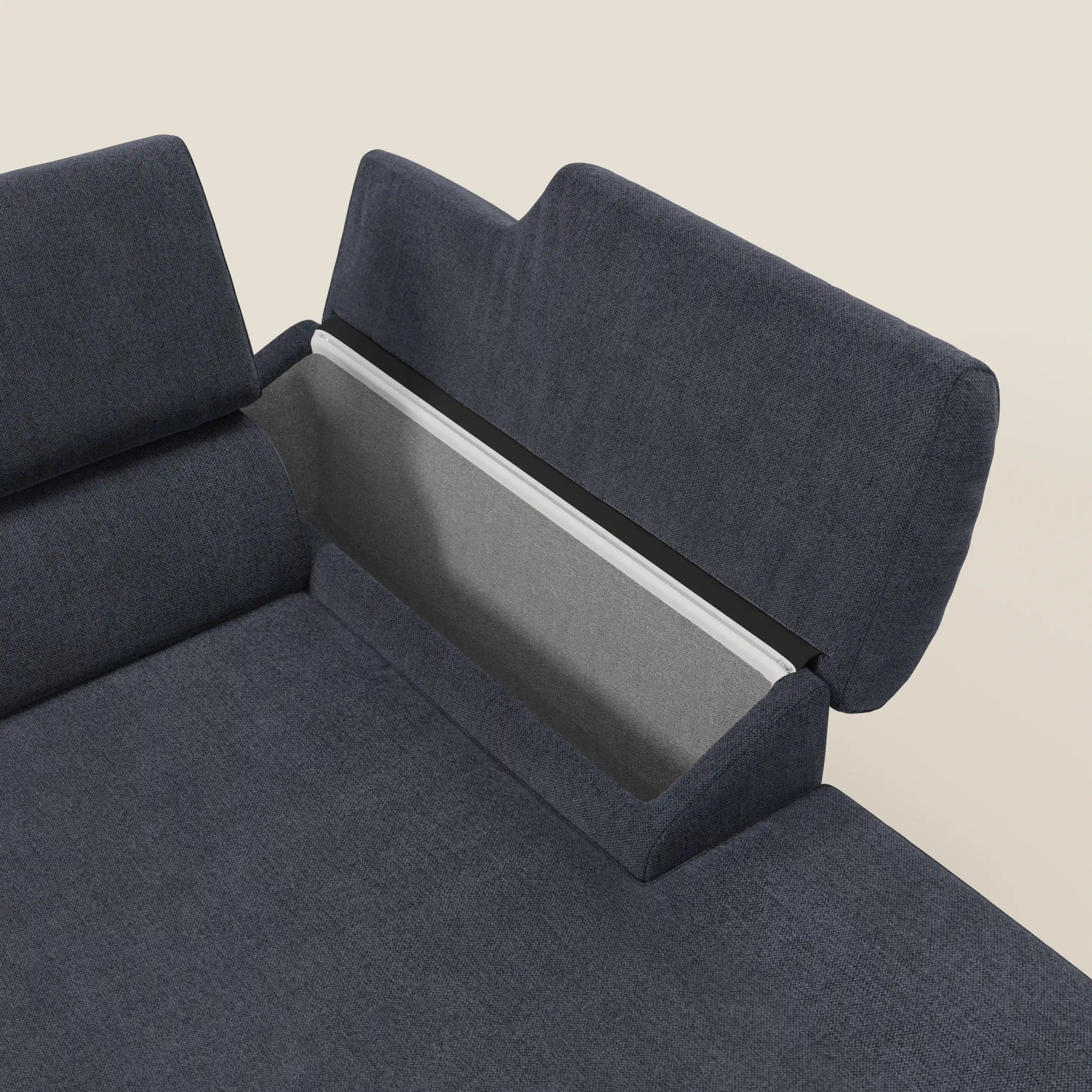 Un primo piano del divano angolare Donatello di Divani.Store in morbido tessuto T23 blu ardesia, facile da pulire, con sedute scorrevoli, braccioli contenitori e poggiatesta su uno sfondo bianco sporco.