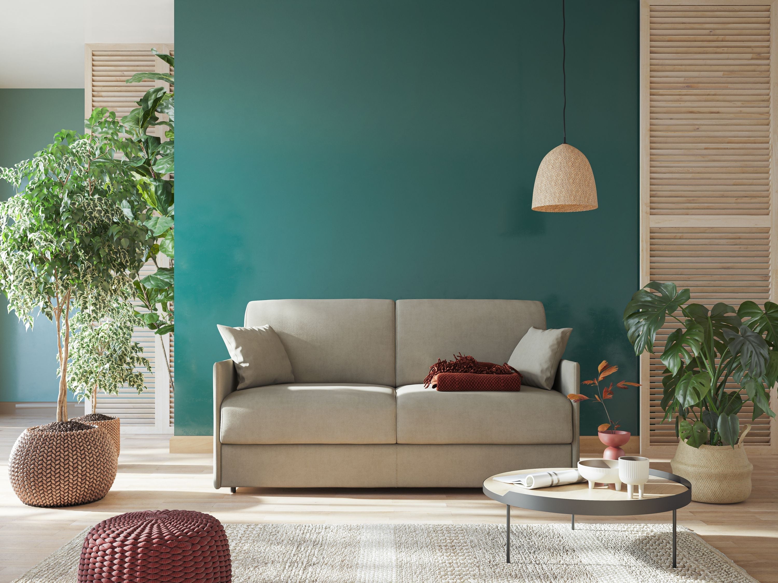 Un soggiorno moderno con divano beige, parete decorativa verde acqua, grandi piante frondose, tavolino rotondo decorato, lampada intrecciata e luce naturale proveniente da sinistra. Arredamento accogliente, minimale ed elegante.