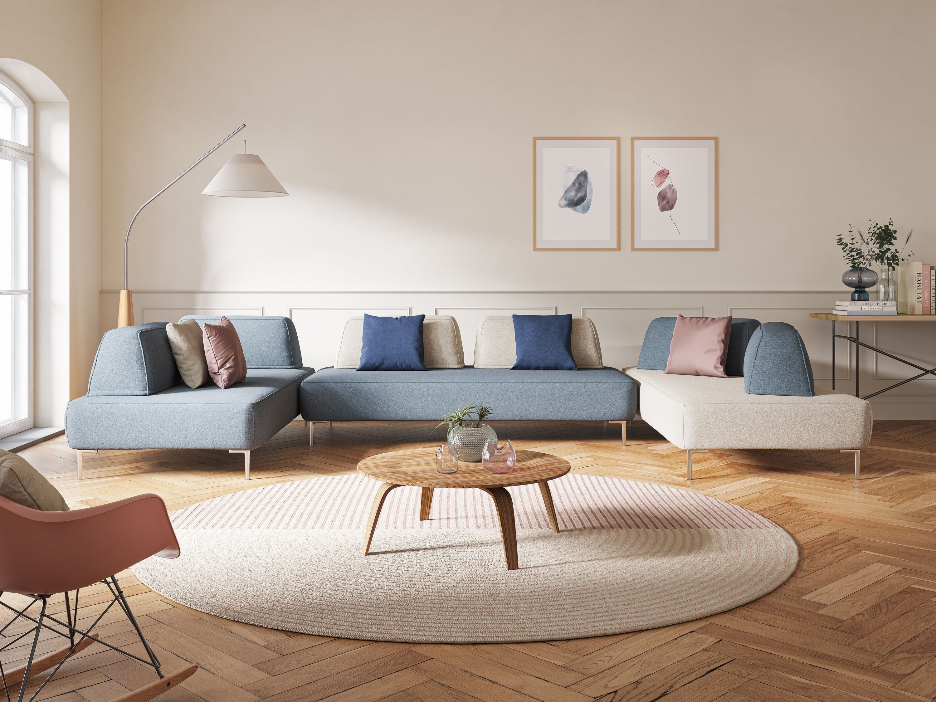Un soggiorno moderno presenta un divano componibile blu e beige con cuscini blu e beige, un tavolino da caffè rotondo in legno, un tappeto a righe, un'opera d'arte da parete incorniciata, una lampada da terra e decorazioni su una consolle.