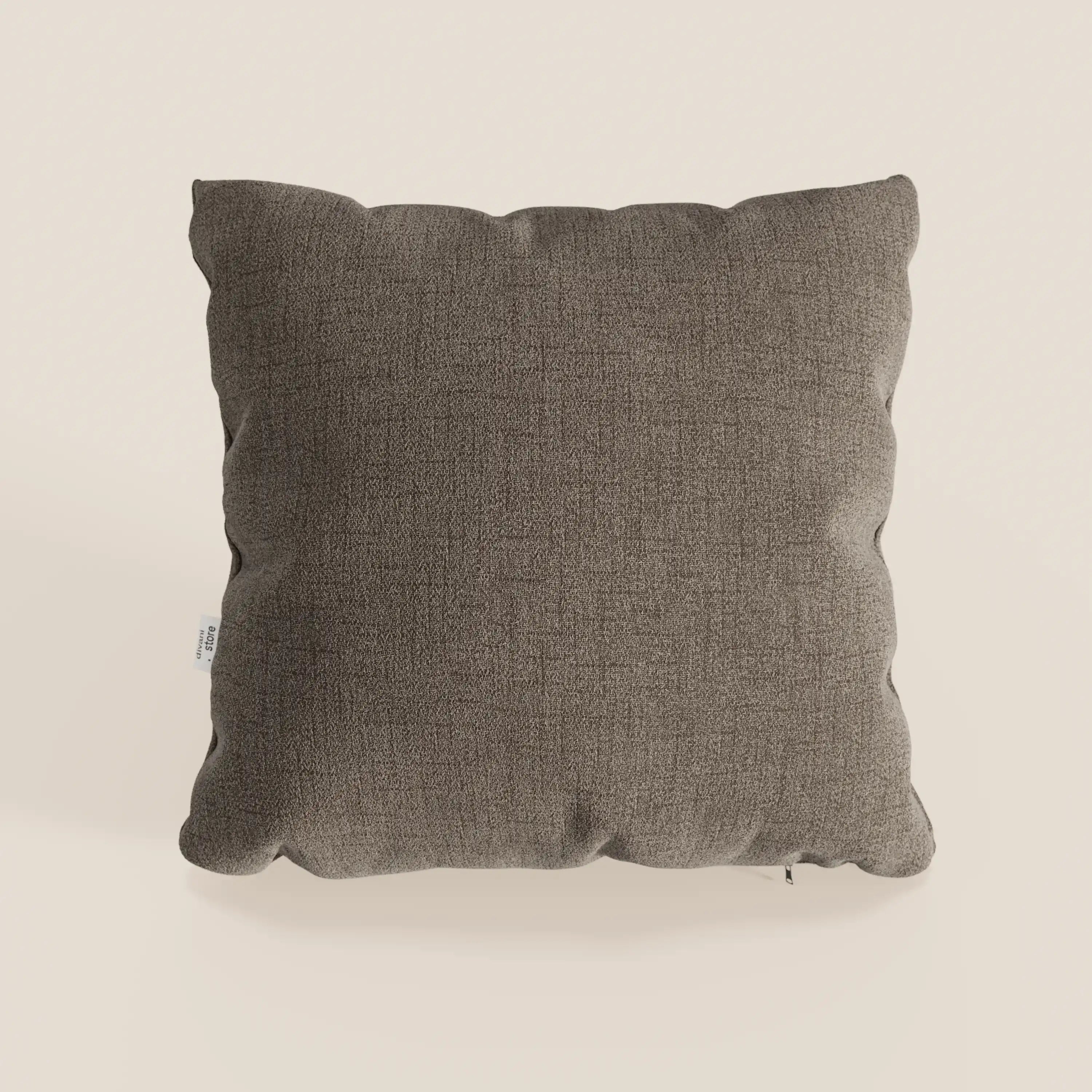 Il cuscino impermeabile Felis T03 marrone di Divani.Store, realizzato in morbido tessuto color tortora scuro, poggia su uno sfondo beige con una sensazione di peluche e una piccola etichetta bianca sulla sinistra.