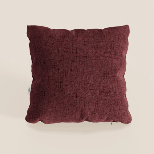 Il cuscino Felis di Divani.Store in rosso T03 è un cuscino quadrato, marrone, impermeabile, con tessuto morbido, superficie strutturata, design minimalista, angoli arrotondati, cuciture a vista e una piccola etichetta bianca sul lato sinistro su sfondo beige.