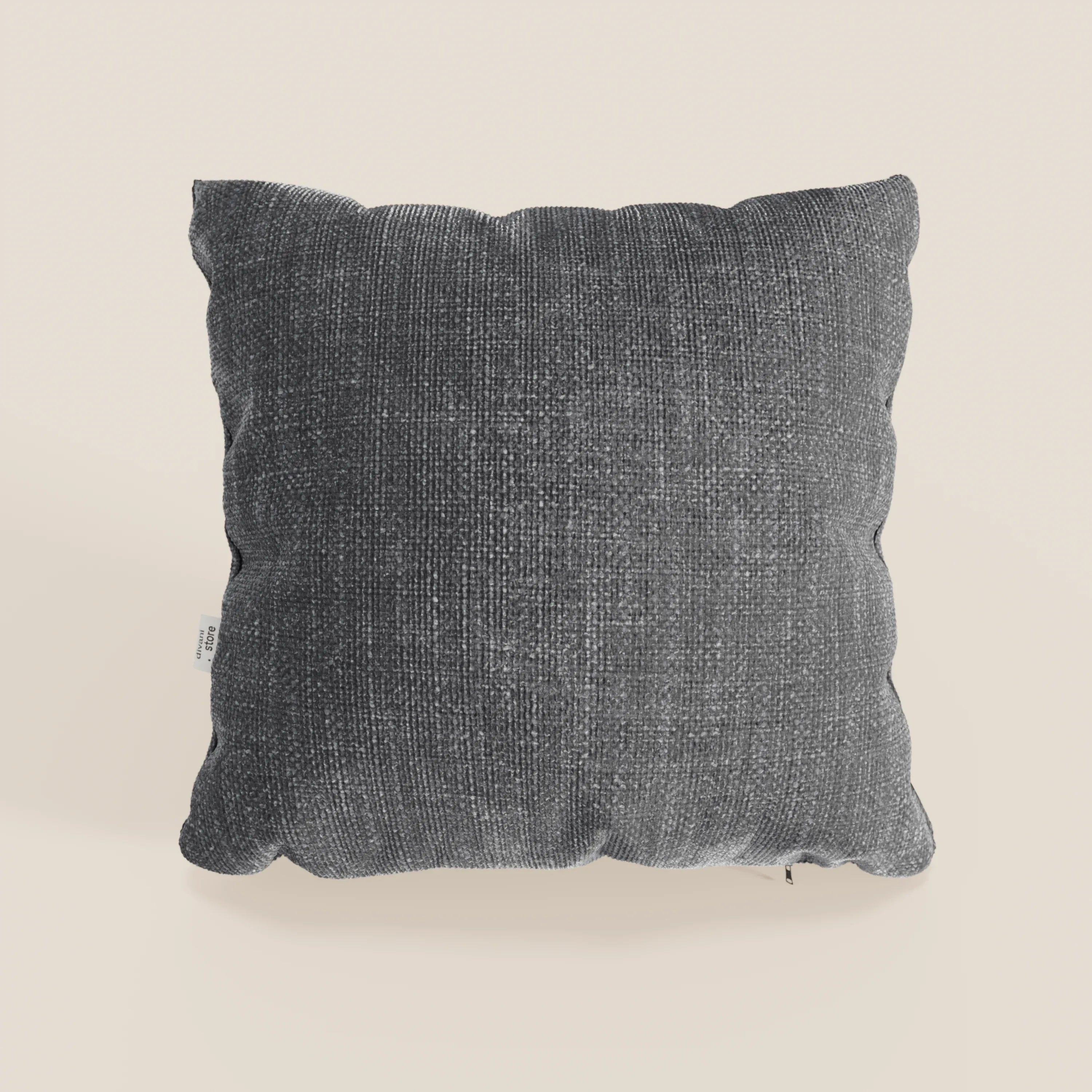 Il cuscino Lyon di Divani.Store, presentato nel colore T06 antracite, è caratterizzato da un morbido tessuto impermeabile intrecciato. Di forma quadrata e dalla texture sottile, presenta una piccola etichetta bianca sul lato ed è esposto su uno sfondo beige chiaro.
