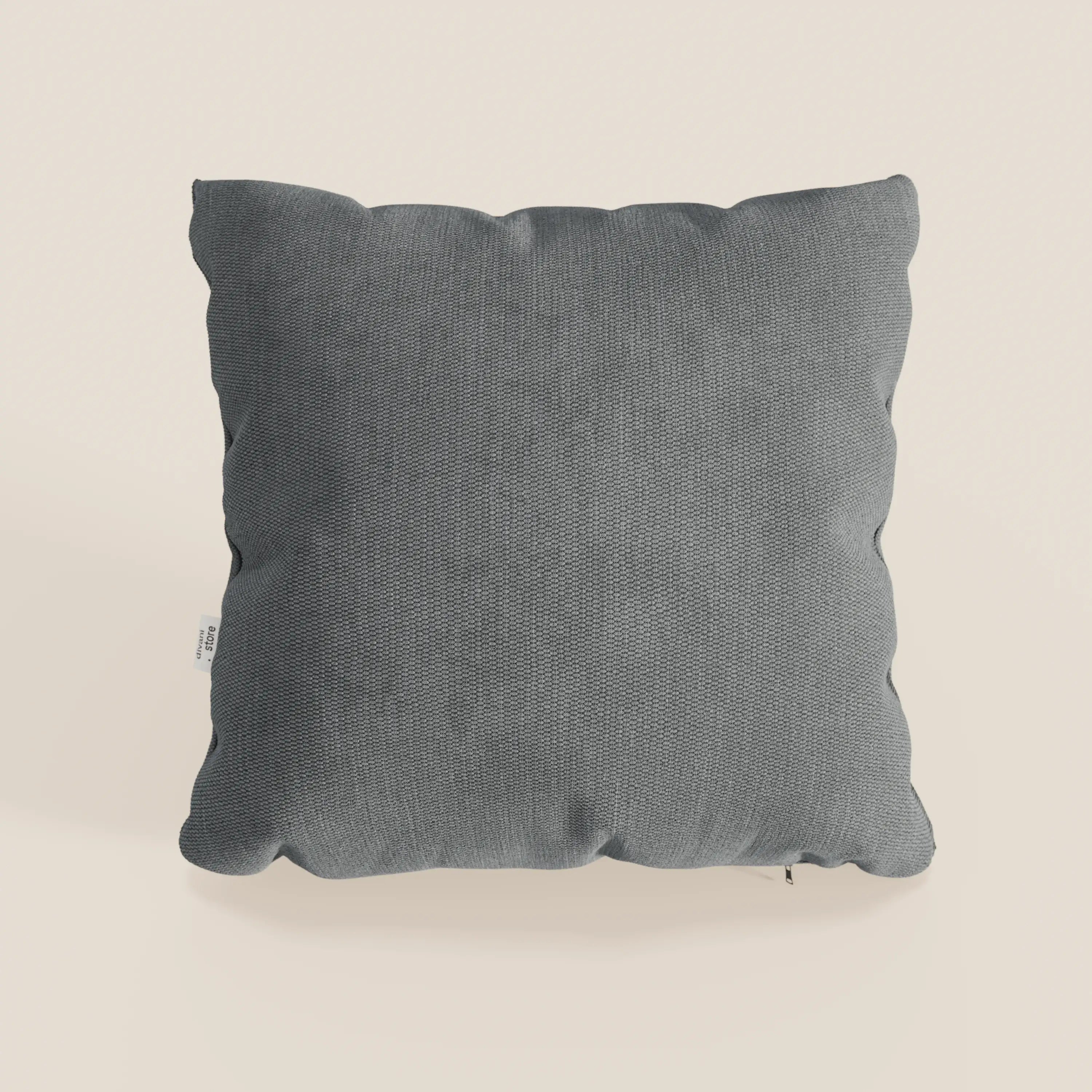 Il cuscino Miami di Divani.Store, in morbido tessuto impermeabile T14 grigio antracite (45x45 cm), presenta una texture sottile, cuciture a vista, bordi leggermente arrotondati e una piccola etichetta bianca, su sfondo beige chiaro.