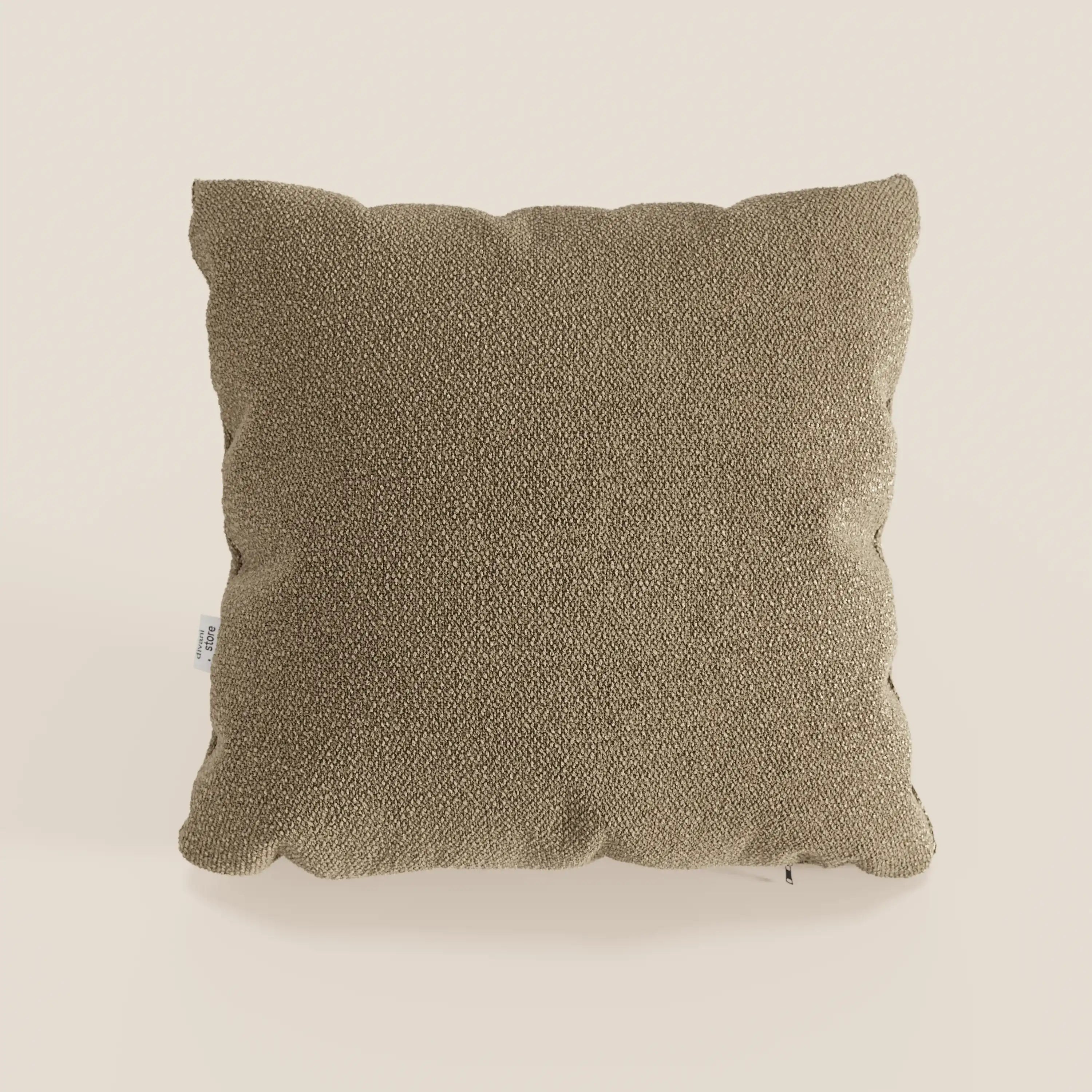 Un cuscino Lambada marrone di Divani.Store, quadrato e strutturato, realizzato in tessuto T33 di cotone naturale, facile da pulire e impermeabile, è centrato su uno sfondo beige semplice. Sul lato sinistro è visibile una piccola etichetta bianca. L'illuminazione è uniforme e neutra.