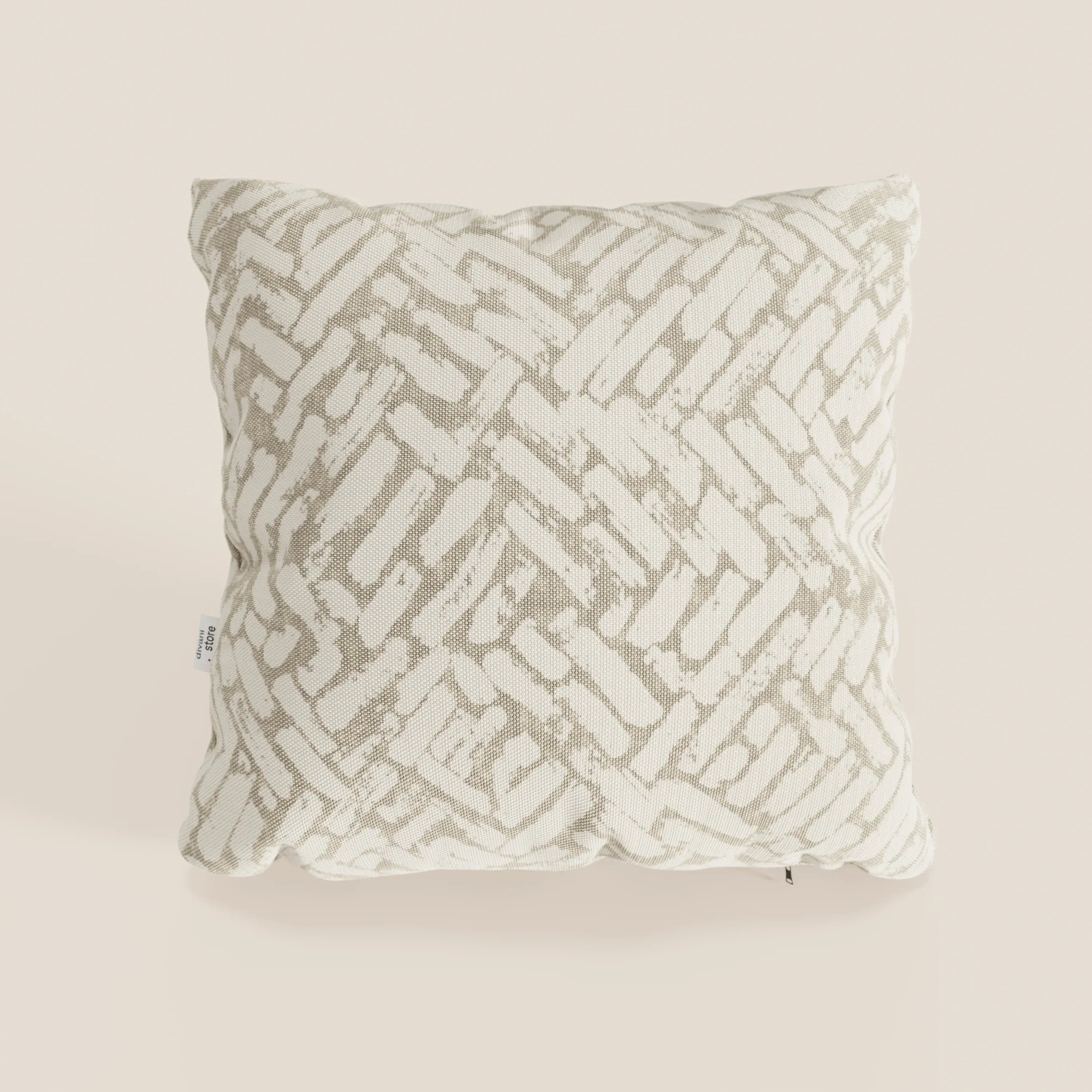 Il cuscino geometrico Brick di Divani.Store è un cuscino decorativo beige, idrorepellente, caratterizzato da un aspetto intrecciato e da linee astratte sovrapposte a pennello per un accento moderno. Include una piccola etichetta bianca sul lato sinistro.