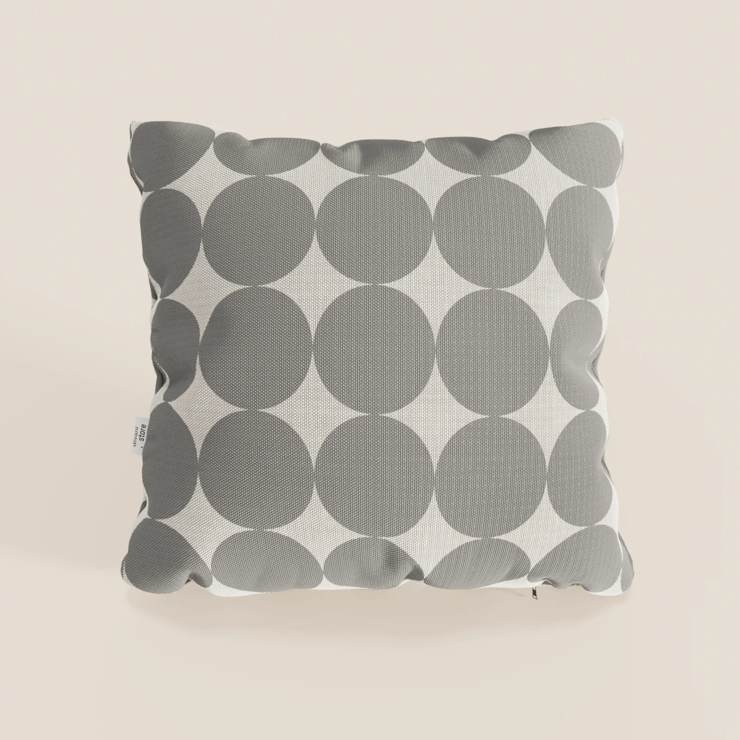 Il cuscino Dot cuscini geometrici di Divani.Store è un cuscino quadrato, idrorepellente, di colore grigio, con grandi cerchi sovrapposti su sfondo bianco, trama del tessuto visibile e una piccola etichetta bianca, su sfondo beige chiaro.