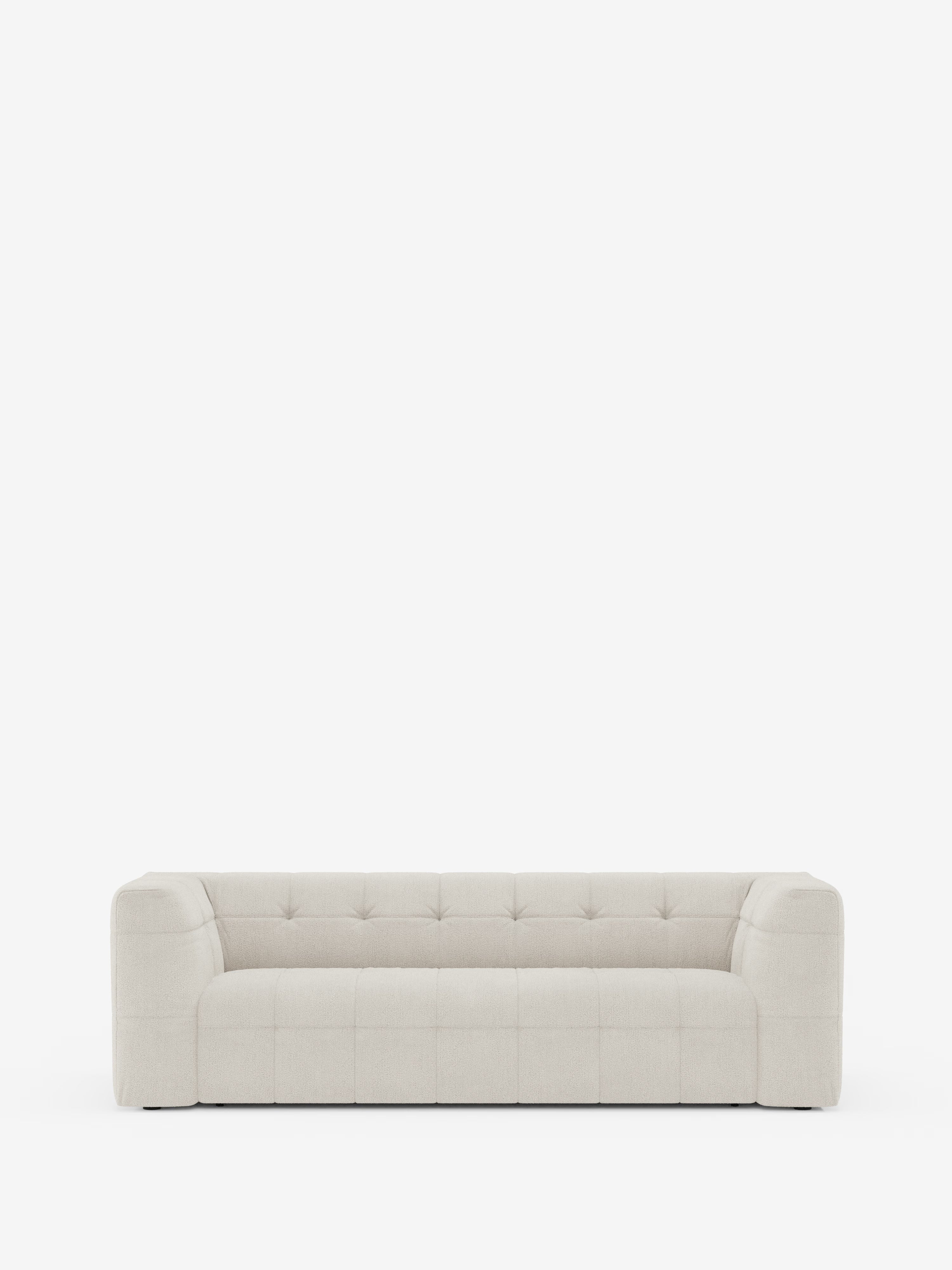 Un moderno divano modulare Mosaic a 3 e 4 posti dal profilo slanciato, realizzato in bouclé: capitonné e design in tessuto antimacchia T21 di Divani.Store, è messo in risalto su uno sfondo bianco a tinta unita. Il design minimalista è caratterizzato da linee pulite, cuscini trapuntati, ampi braccioli e un morbido tessuto antimacchia.