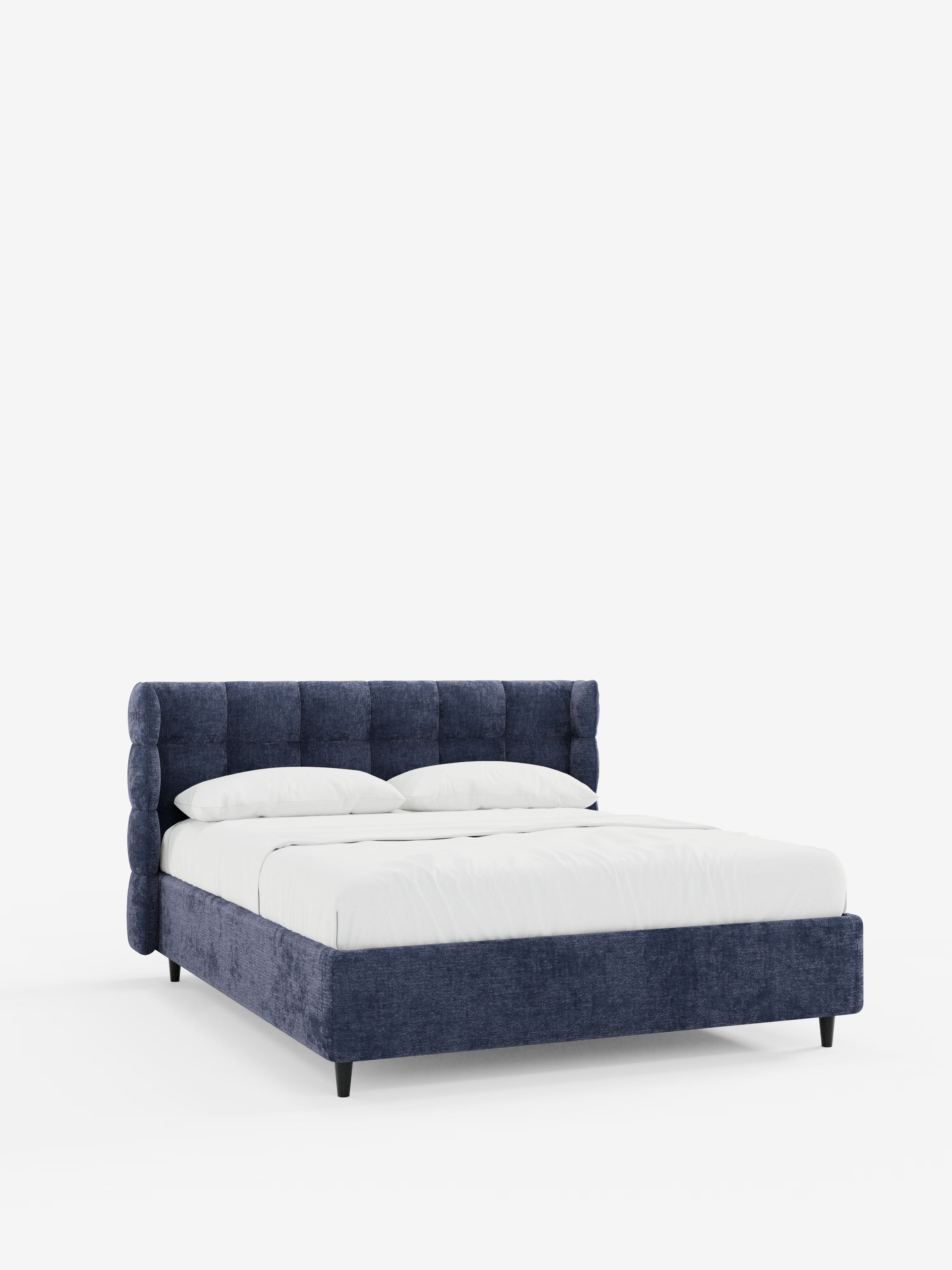 Il letto imbottito RAGNAR con contenitore e testiera capitonné avvolgente di Letti.store presenta una struttura contemporanea rivestita in blu navy con un elegante tessuto certificato Oeko-Tex®. La sua raffinata testiera capitonné si abbina a gambe minimaliste di colore nero, mentre la biancheria da letto e i cuscini di un bianco candido completano il look su uno sfondo bianco a tinta unita.