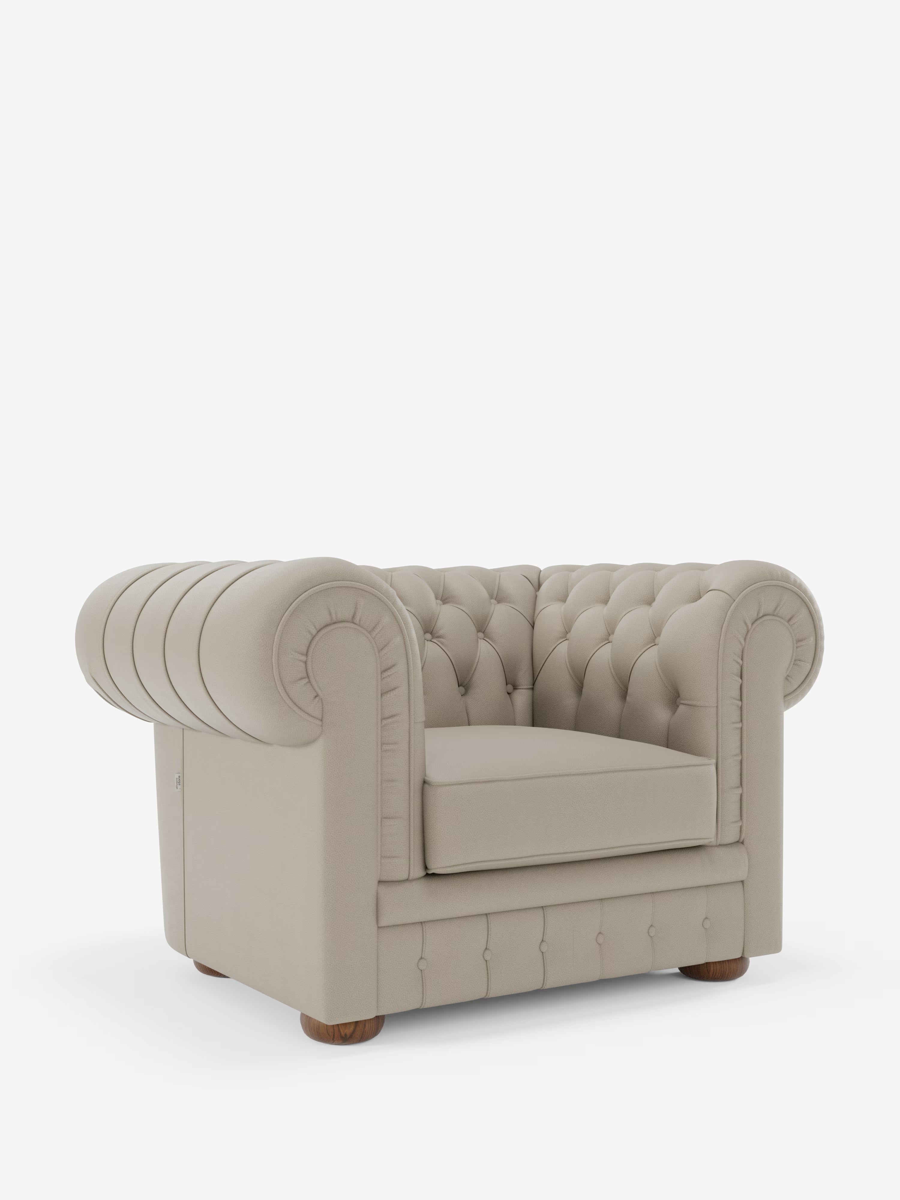 Una poltrona Chester in vera pelle spessorata con capitonné artigianale di Divani.Store — una poltrona Chesterfield beige con capitonné, braccioli arrotondati, profondi bottoni decorativi e piedini in legno — è esposta su uno sfondo bianco a tinta unita.