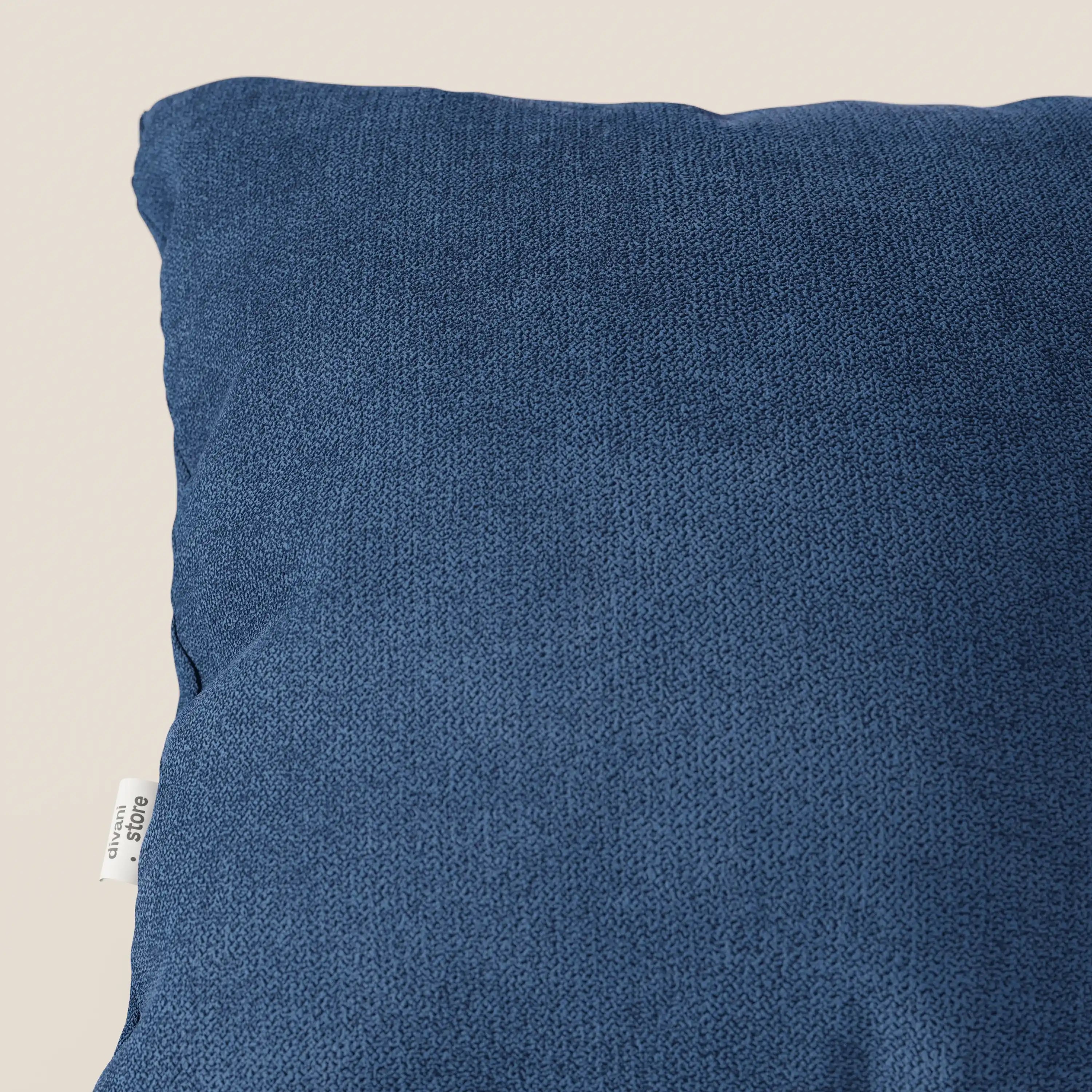 Primo piano del cuscino Destiny 45x45 di Divani.Store in T02 blu, caratterizzato da un morbido tessuto impermeabile. Il cuscino è parzialmente rappresentato con una piccola etichetta in tessuto bianco con testo nero sulla cucitura sinistra, su uno sfondo bianco sporco.