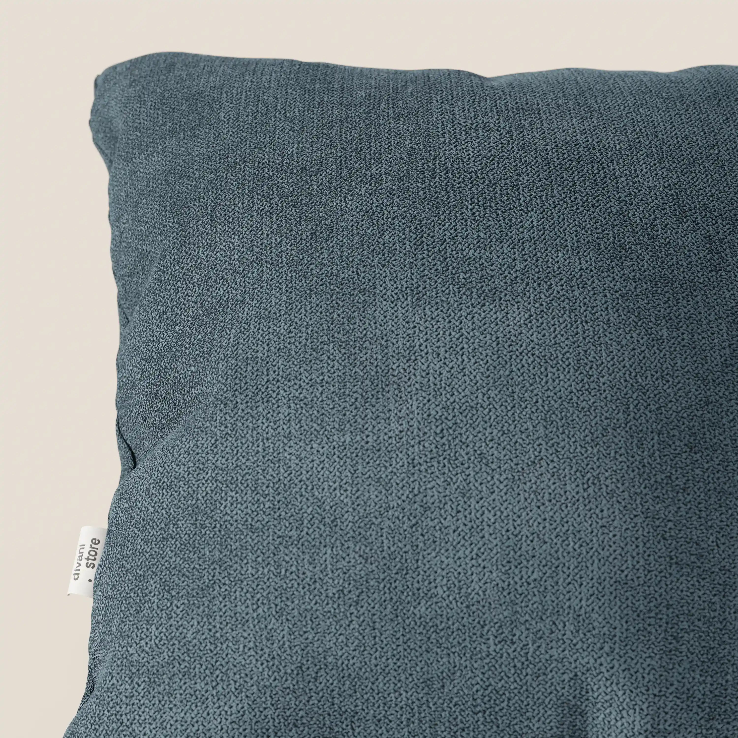 Primo piano del cuscino Destiny 45x45 cm di Divani.Store in tessuto morbido impermeabile T02 petrolio, disponibile in vari colori, con fodera lavabile e una piccola etichetta bianca a sinistra, su sfondo beige chiaro.