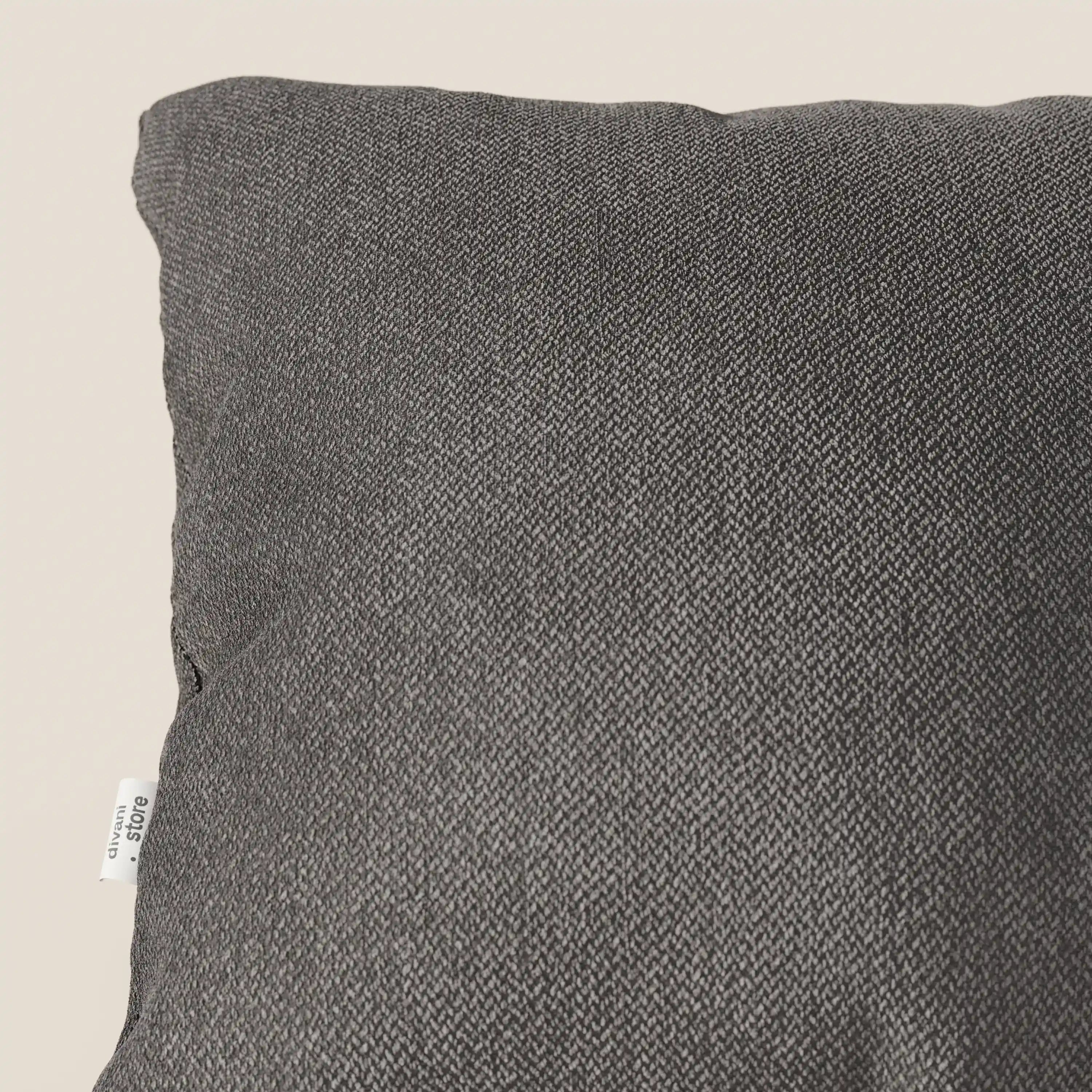 Primo piano dell'angolo superiore sinistro di un cuscino Sogno di Divani.Store in tessuto morbido SMACCHIABILE T05 antracite, su uno sfondo beige chiaro. Una piccola etichetta bianca con la scritta nera "&C URBAN" è cucita nella cucitura laterale di questo elegante cuscino.