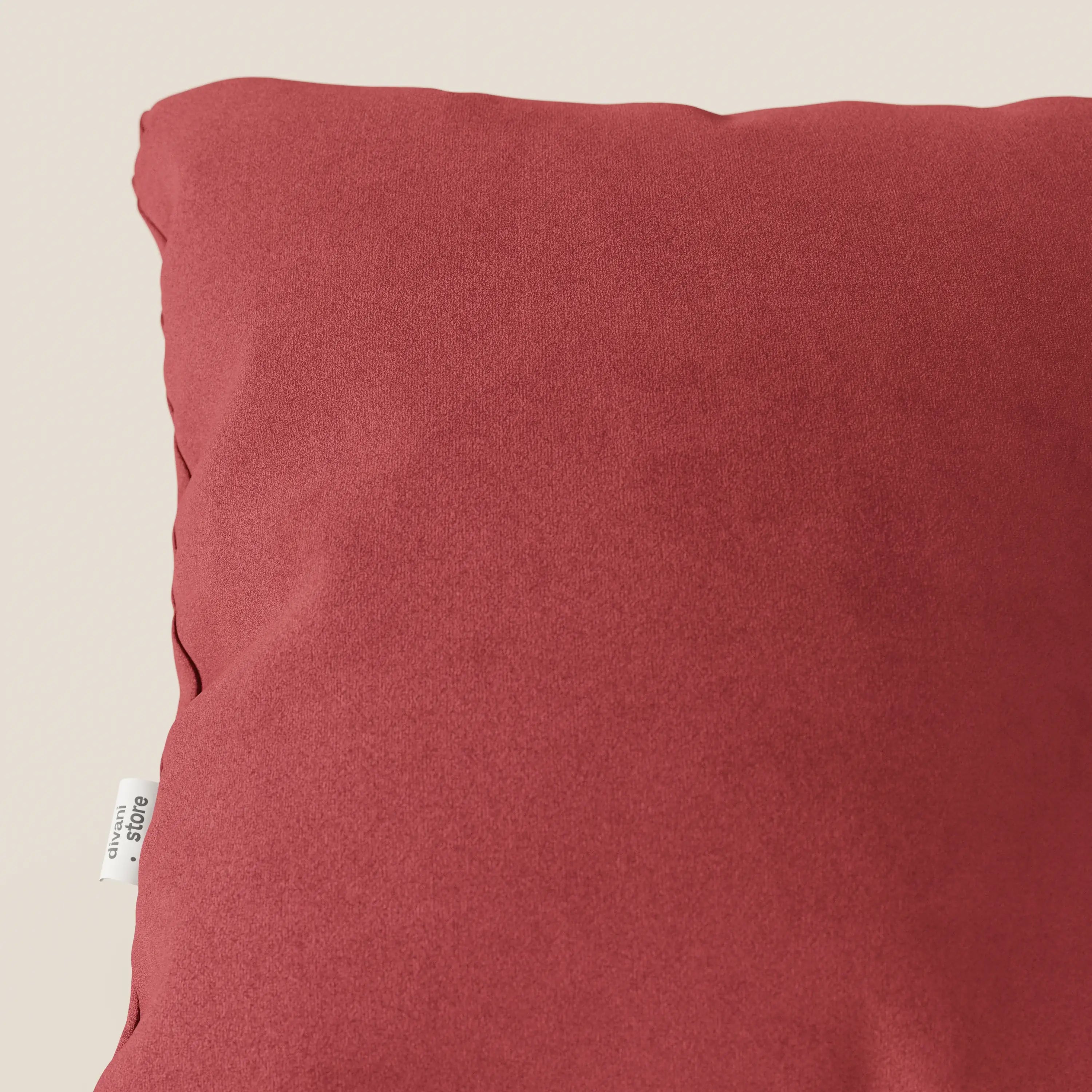 Primo piano del cuscino Jazz di Divani.Store in microfibra tecnica smacchiabile T11 rosso, caratterizzato da una forma morbida e quadrata con una texture liscia e una piccola etichetta bianca sul lato. Lo sfondo è un semplice color crema chiaro.