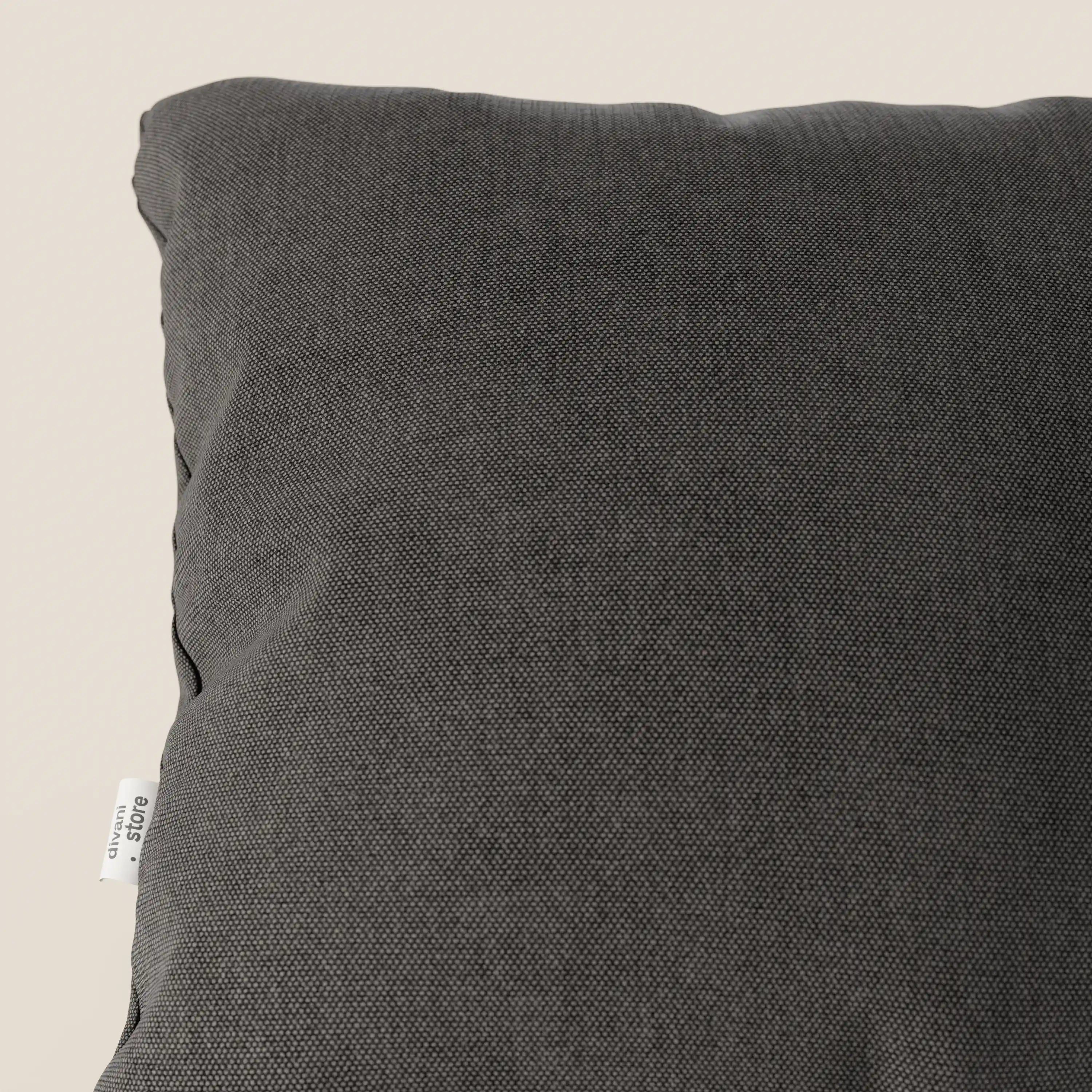 Primo piano del cuscino Honey 45x45 di Divani.Store in T13 antracite, realizzato in morbido tessuto simil cotone impermeabile. Il cuscino presenta una piccola etichetta bianca sulla cucitura laterale della fodera lavabile e si presenta su uno sfondo beige chiaro.