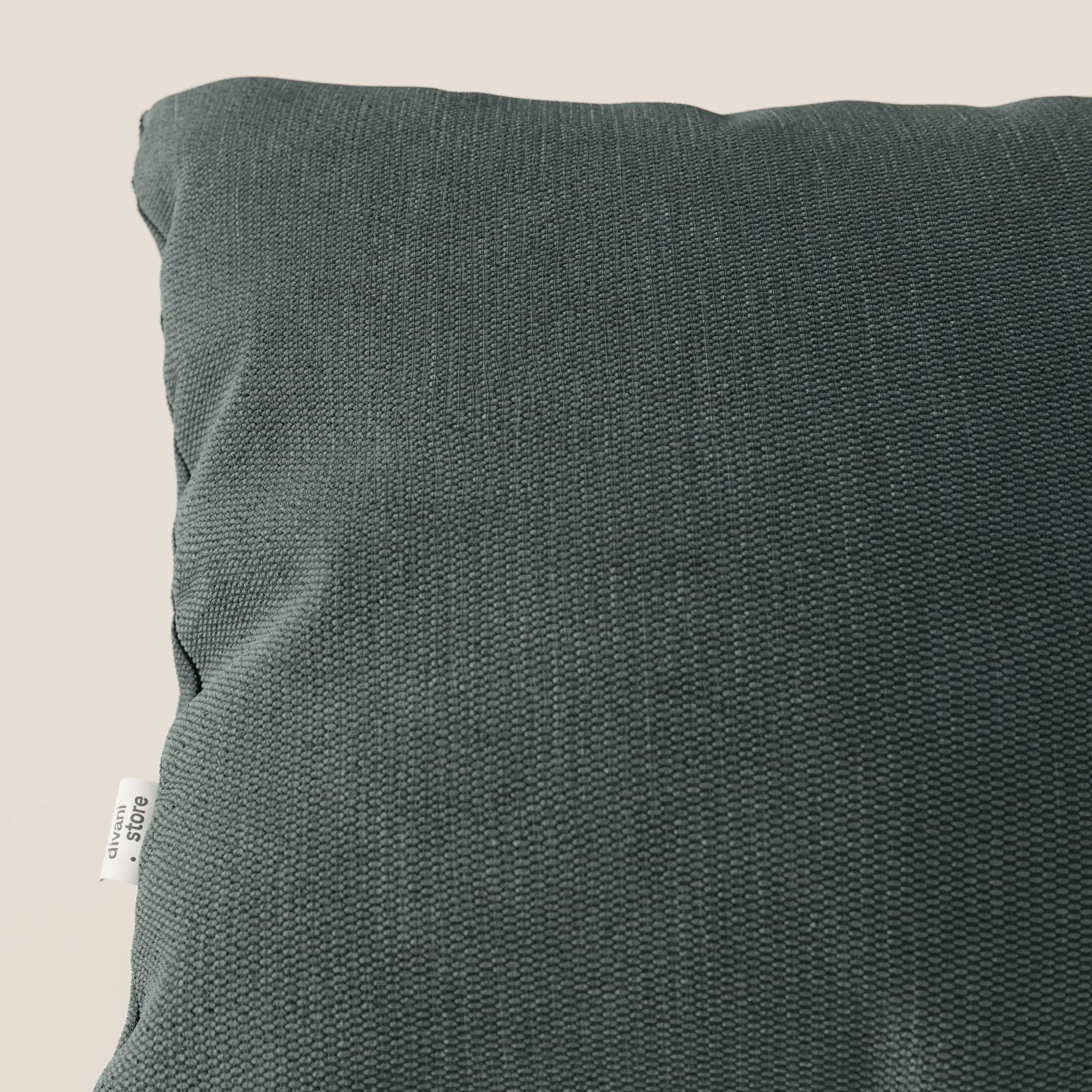 Primo piano di un cuscino Miami 45x45 cm T14 verde di Divani.Store, in morbido tessuto impermeabile con rivestimento soft-touch, trama intrecciata ed etichetta bianca a vista su sfondo beige chiaro.