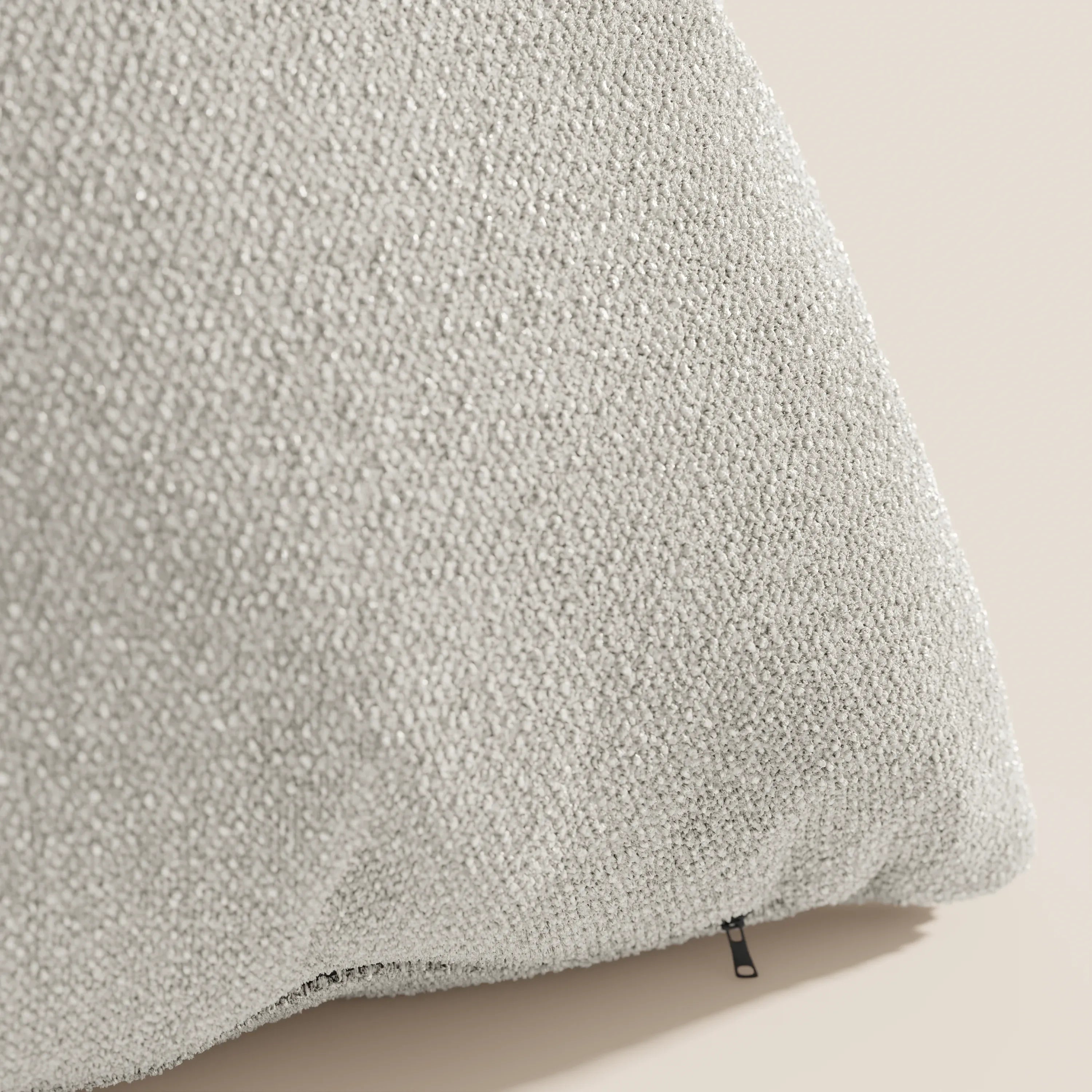 Primo piano del cuscino Lambada di Divani.Store in grigio chiaro, caratterizzato da un sottile motivo a bouclé in rilievo su tessuto smacchiabile e impermeabile in cotone T33. La cerniera è leggermente visibile; lo sfondo è beige tenue.