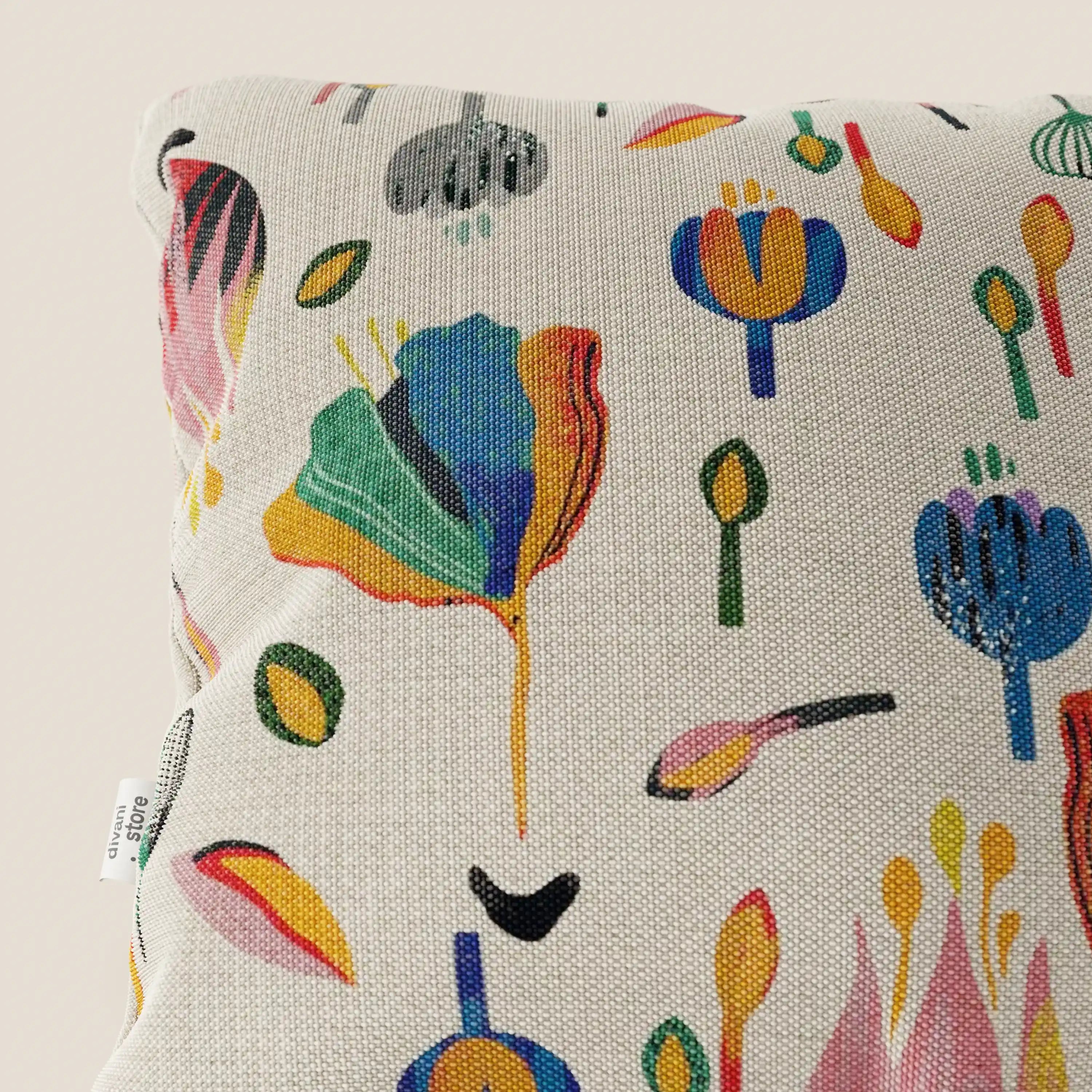 Un primo piano del cuscino Divani.Store Joy collezione 45x45 cm mostra la sua fantasia floreale astratta multicolore su un fresco cotone panna impermeabile. Un cartellino in tessuto bianco si trova sul lato, su uno sfondo chiaro e neutro.