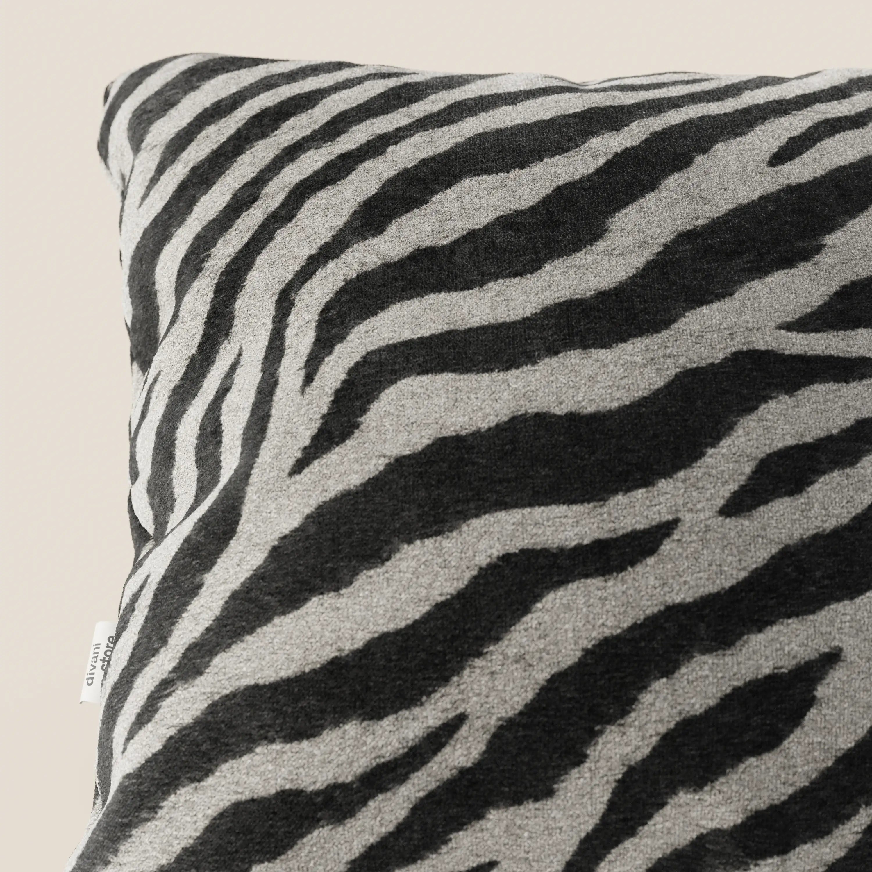 Un primo piano del cuscino Wild 45x45 della collezione Wild di Divani.Store mostra il suo tessuto in microfibra impermeabile zebrata nera e grigia con una piccola etichetta bianca sulla cucitura sinistra, su uno sfondo beige chiaro.