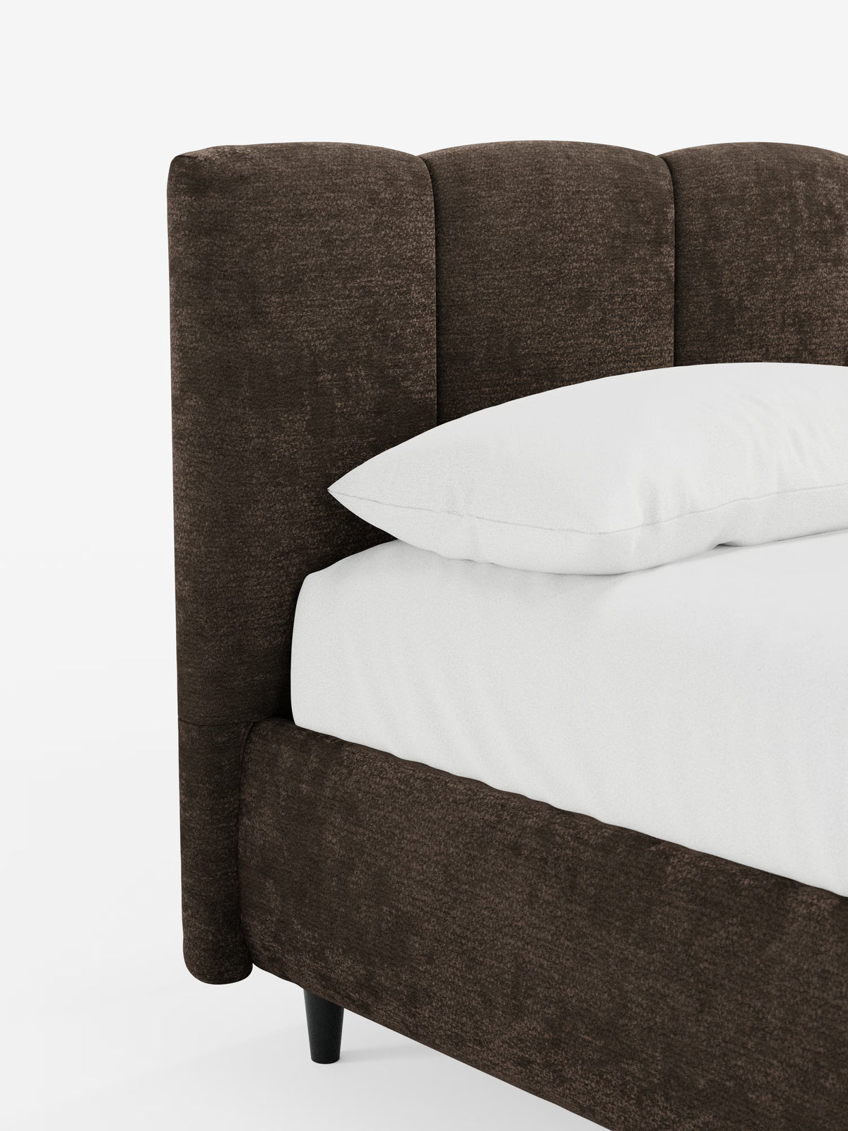 Primo piano del letto imbottito ARKAM con contenitore e testiera a cuciture verticali di Letti.store, caratterizzato da una struttura imbottita color marrone scuro in tessuto certificato Oeko-Tex® con una testiera morbida e impreziosita da cuciture verticali. Un cuscino bianco e un lenzuolo con angoli ricoprono il materasso, creando un contrasto suggestivo con il tessuto scuro. La struttura poggia su corte gambe nere ed è raffigurata su uno sfondo bianco a tinta unita.