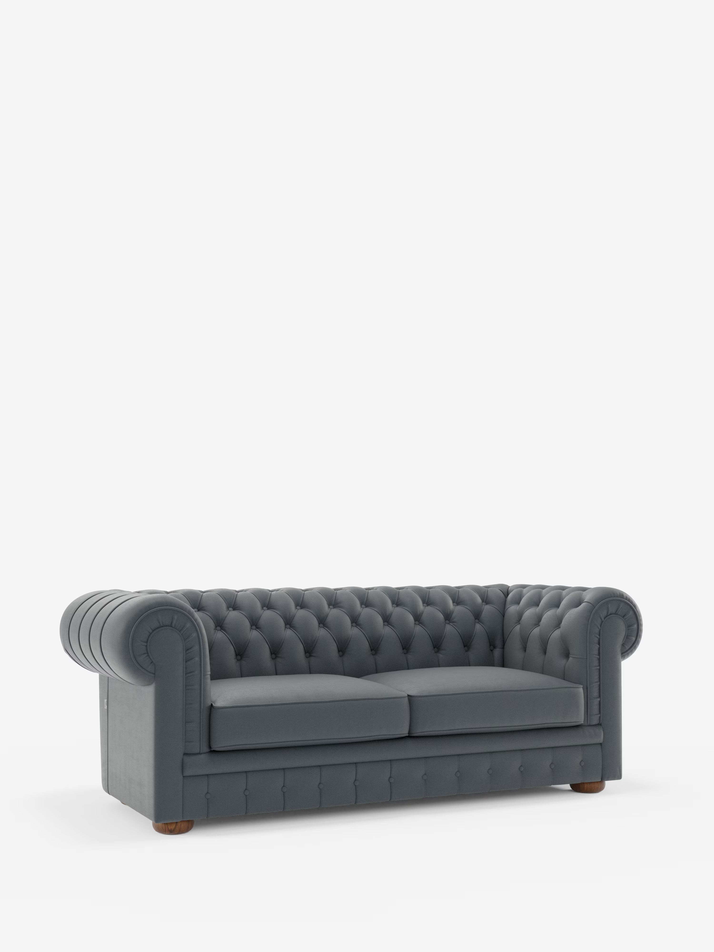 Un divano Chesterfield grigio scuro con rivestimento a ciuffetti – Divano Chesterfield in vera pelle spessorata a 2 e 3 posti di Divani.Store, con braccioli arrotondati e gambe basse in legno – spicca su uno sfondo bianco a tinta unita. Questo divano artigianale di produzione italiana è dotato di due cuscini di seduta e si distingue per il suo design classico ed elegante.