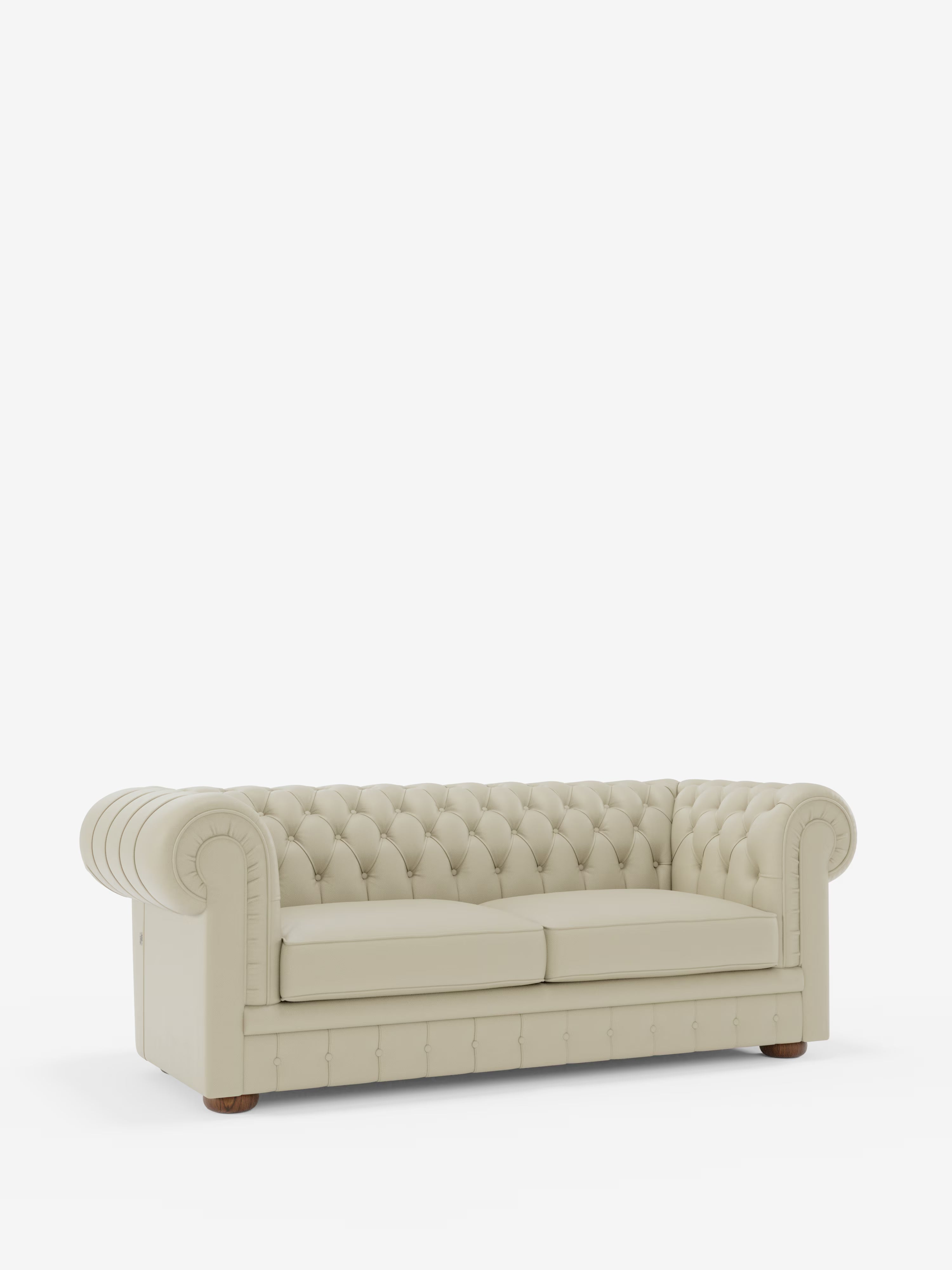Un classico ed elegante Chesterfield color crema: il divano Chesterfield in vera pelle spessorata a 2 e 3 posti di Divani.Store, caratterizzato da una profonda trapuntatura a bottoni, braccioli arrotondati, cuscini rettangolari spessi e piedini in legno. Il divano è esposto su uno sfondo bianco.