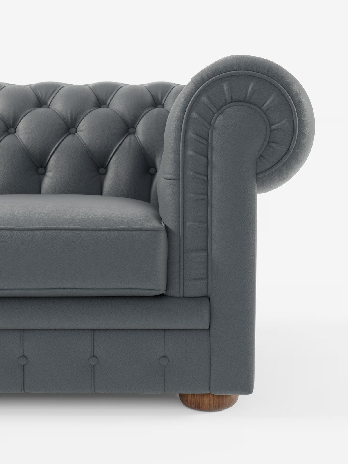 Un primo piano del divano Chester 4 Posti 3 sedute in Vera Pelle – Chesterfield Capitonné Artigianale di Divani.Store, che ne mette in risalto il rivestimento in vera pelle capitonné grigio scuro, i braccioli arrotondati, i dettagli a bottoni e una parte del cuscino di seduta. Il divano, realizzato artigianalmente, presenta gambe in legno ed è posizionato su uno sfondo bianco a tinta unita.