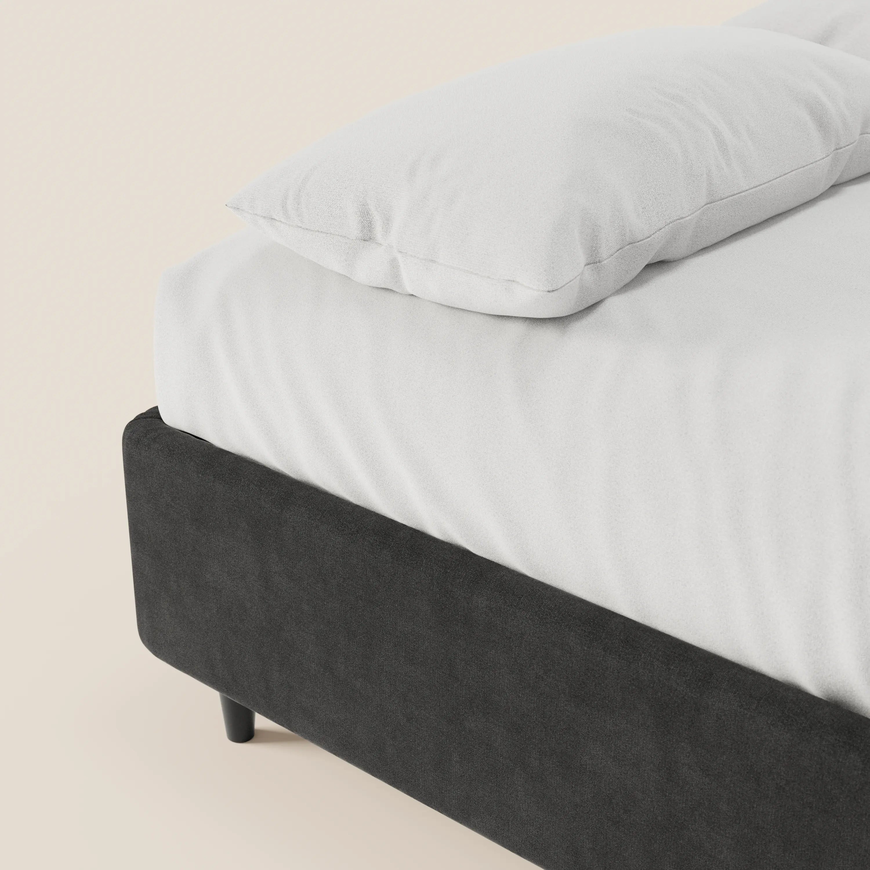 Un primo piano del letto sommier imbottito ERON di Letti.store, con un cuscino bianco e un lenzuolo con angoli su un letto nero in tessuto impermeabile certificato Oeko-Tex dotato di contenitore; lo sfondo beige chiaro ne esalta il design pulito e moderno.