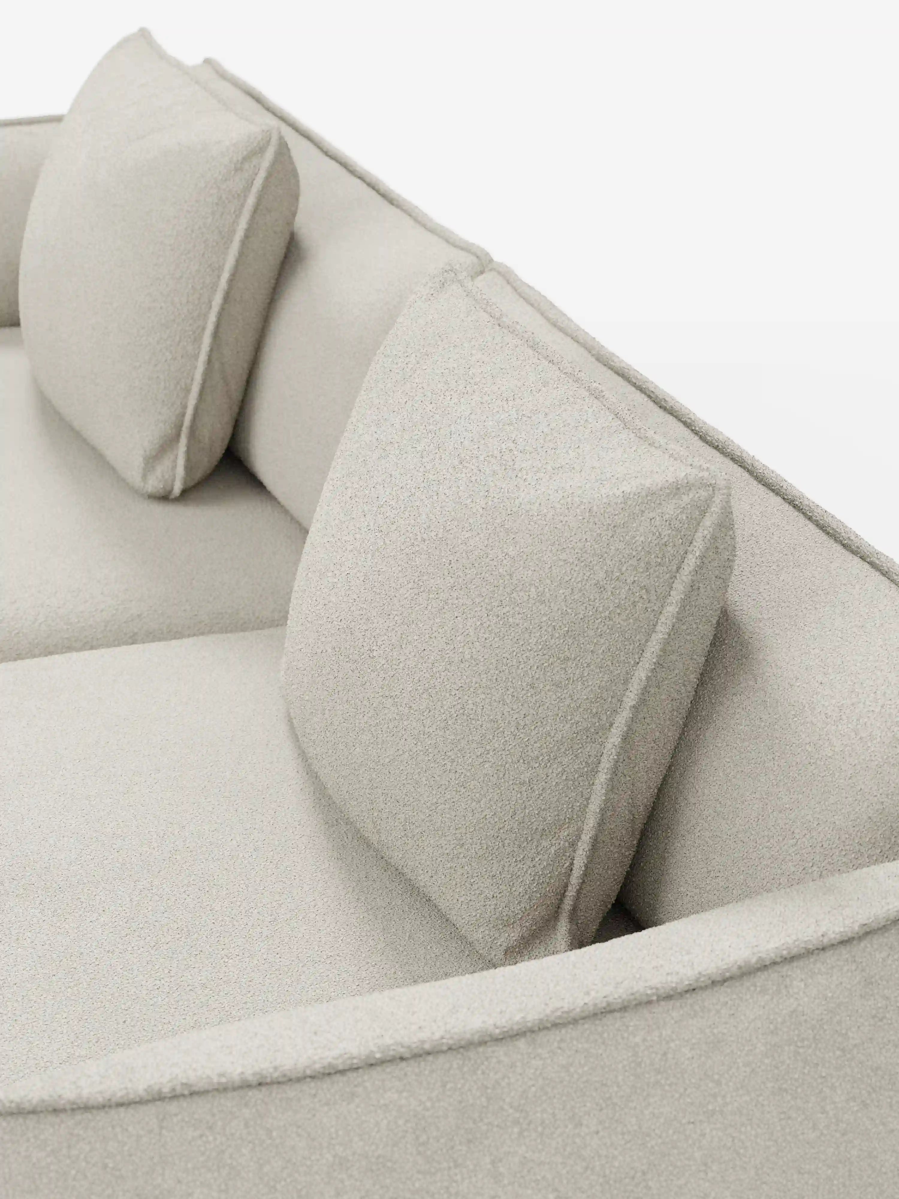 Un primo piano del divano modulare e componibile a 3 posti Nimbus da 250 cm di Divani.Store, un elegante divano modulare beige chiaro rivestito in tessuto smacchiabile effetto cotone T33. Questo modello sfoderabile presenta due cuscini quadrati coordinati per lo schienale, linee pulite e minimaliste e una seduta morbida con rivestimento testurizzato che unisce eleganza e praticità, il tutto su uno sfondo bianco.