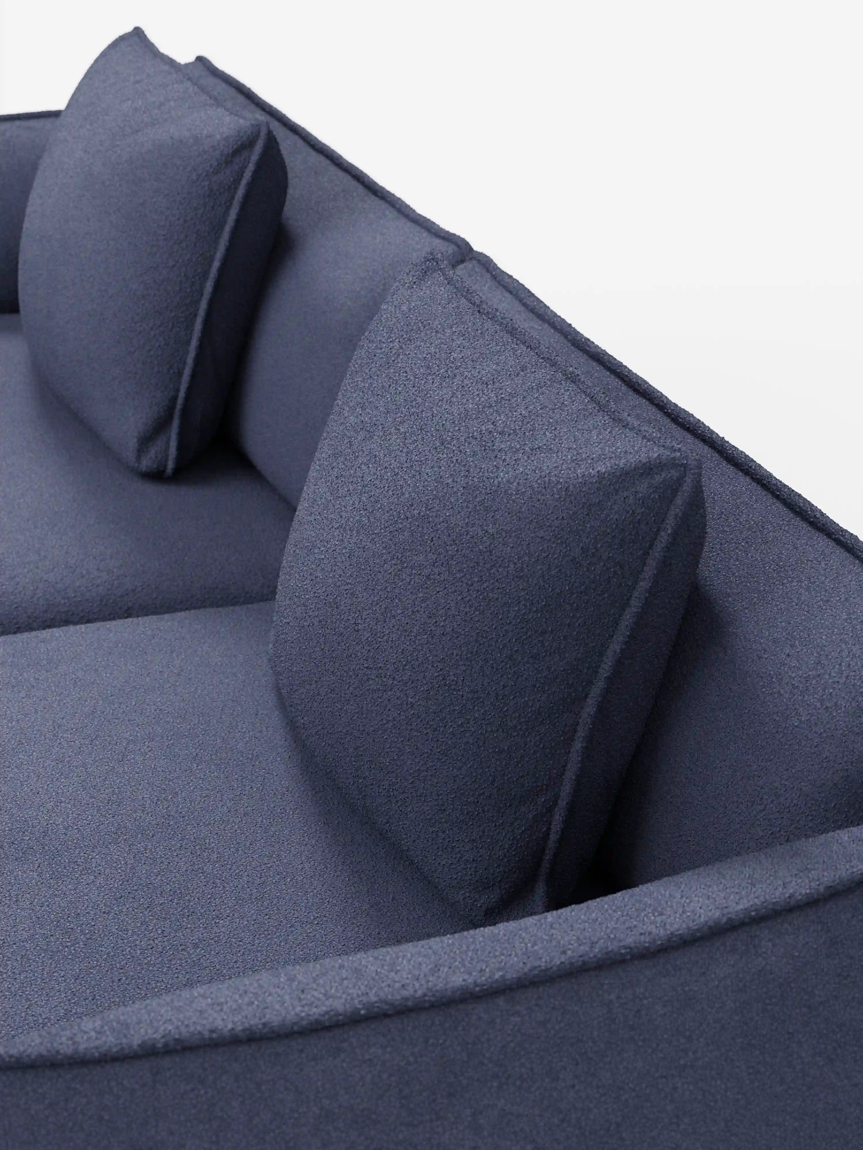 Una vista ravvicinata dall'alto del divano modulare e componibile Nimbus di Divani.Store, a 3 posti, da 250 cm, in blu scuro, rivestito in tessuto lavabile e antimacchia effetto cotone t33. Questo divano moderno presenta un design minimalista dalle linee pulite, un rivestimento liscio, braccioli leggermente arrotondati ed è dotato di due cuscini quadrati coordinati per lo schienale, il tutto su uno sfondo bianco a tinta unita.