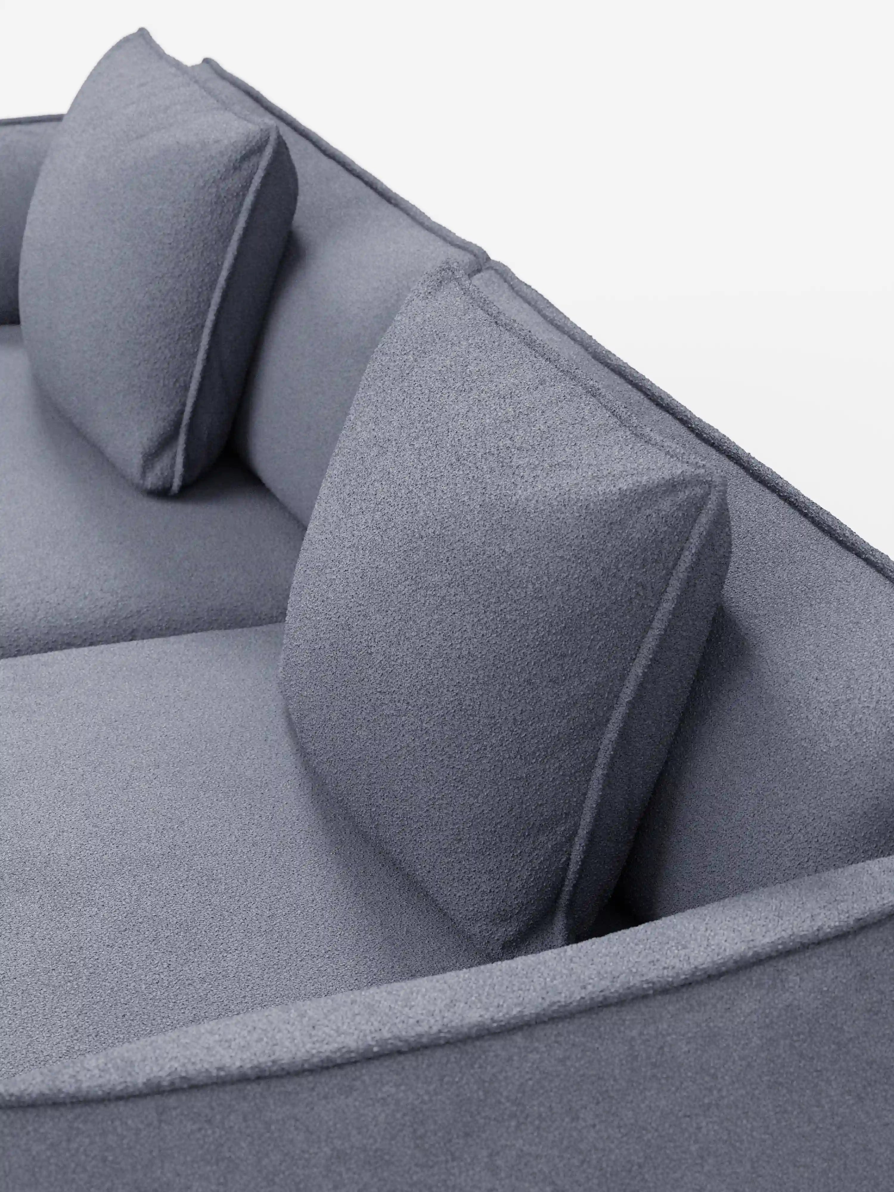 Un primo piano del divano modulare e componibile a 3 posti Nimbus di Divani.Store, da 250 cm, presentato in un moderno tessuto effetto cotone di colore grigio chiaro resistente alle macchie (t33), caratterizzato da due cuscini dello schienale quadrati e braccioli arrotondati su uno sfondo bianco. Il rivestimento sfoderabile appare morbido, accentuando il design minimalista e contemporaneo del divano.