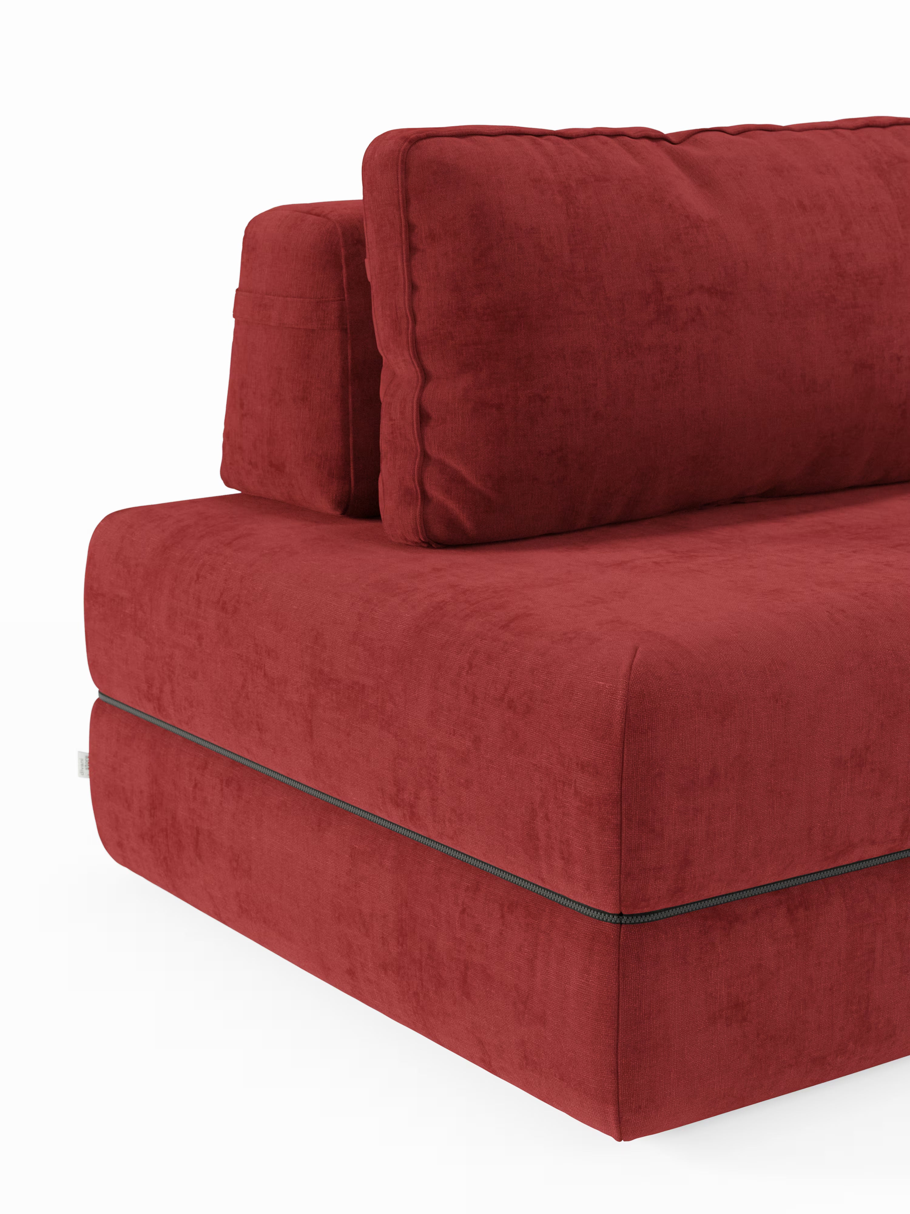 Primo piano di un moderno divano letto matrimoniale Rift di Divani.Store, qui presentato in un tessuto rosso intenso dalla trama morbida. L'attenzione è concentrata sull'angolo sinistro, che mette in risalto i cuscini spessi della seduta e dello schienale con sottili dettagli di cucitura, nonché una cerniera orizzontale a vista vicino al bordo inferiore che consente di accedere facilmente al materasso in memory foam da 22 cm di altezza, modello T31, nascosto al suo interno. Sfondo bianco.