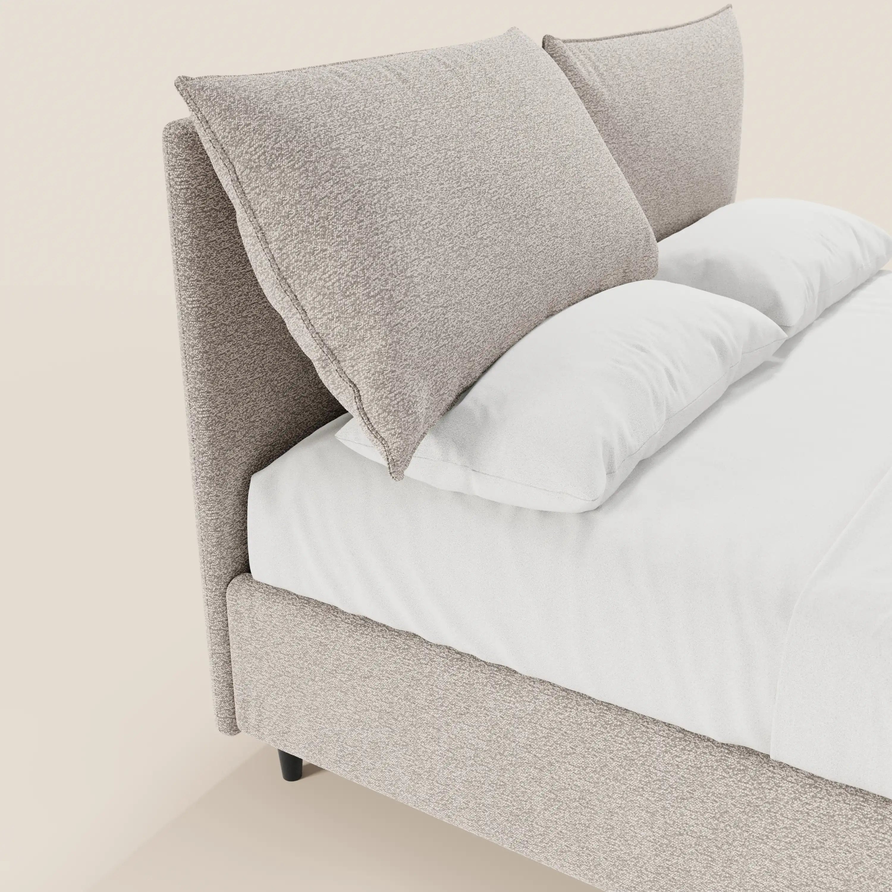 Un primo piano del letto imbottito ZAYRON di Letti.store mette in risalto la struttura in tessuto beige chiaro certificato Oeko-Tex® e la testata regolabile con due grandi cuscini testurizzati, oltre ai cuscini bianchi su un letto rifatto con cura e dotato di vano contenitore.