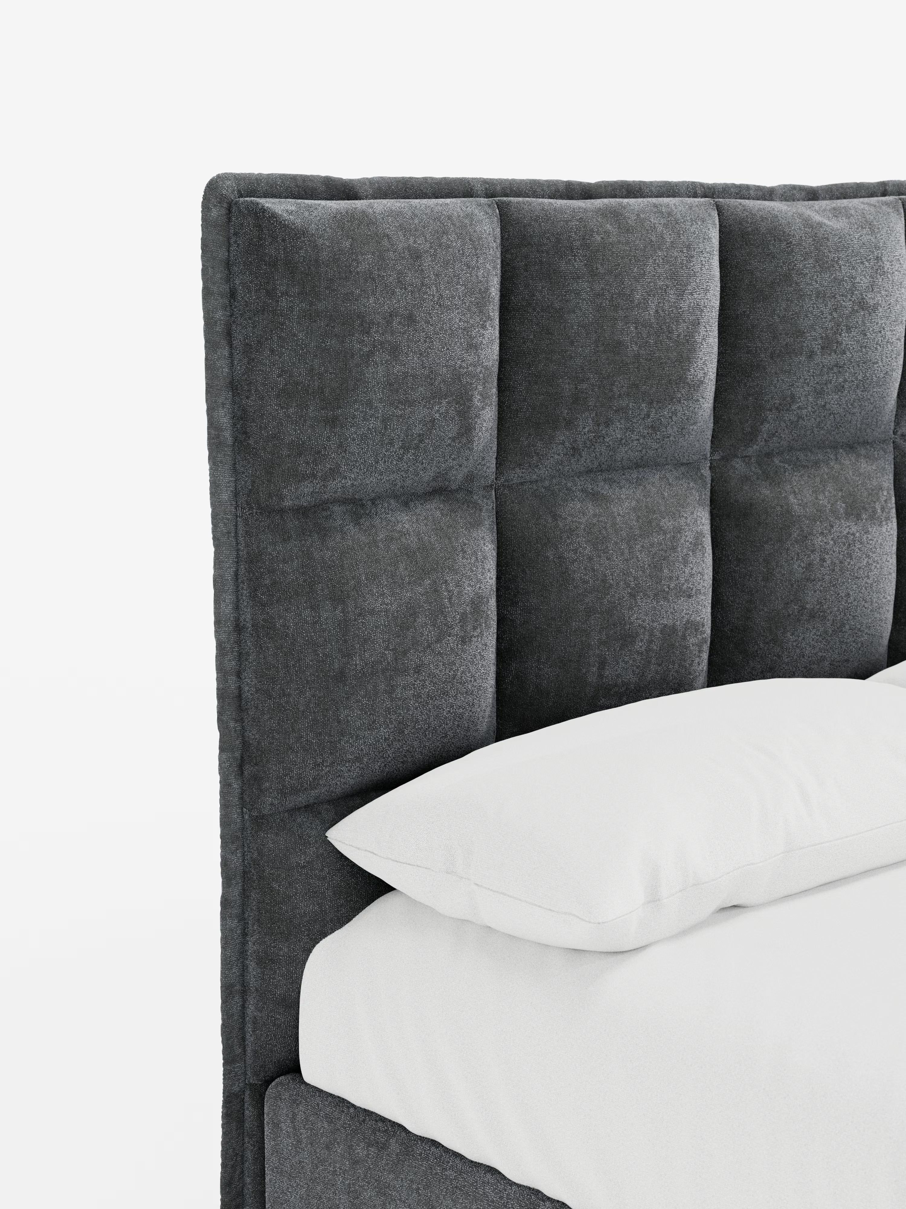 Un primo piano del letto imbottito AURO con contenitore e testiera capitonné alta in ciniglia Oeko-Tex® di Letti.store mette in risalto la sua elegante testiera grigia in tessuto capitonné, caratterizzata da una finitura morbida e strutturata e da cuciture a vista che formano un raffinato motivo a quadrati. Il letto è abbinato a un cuscino bianco e a biancheria da letto bianca, su uno sfondo bianco a tinta unita.