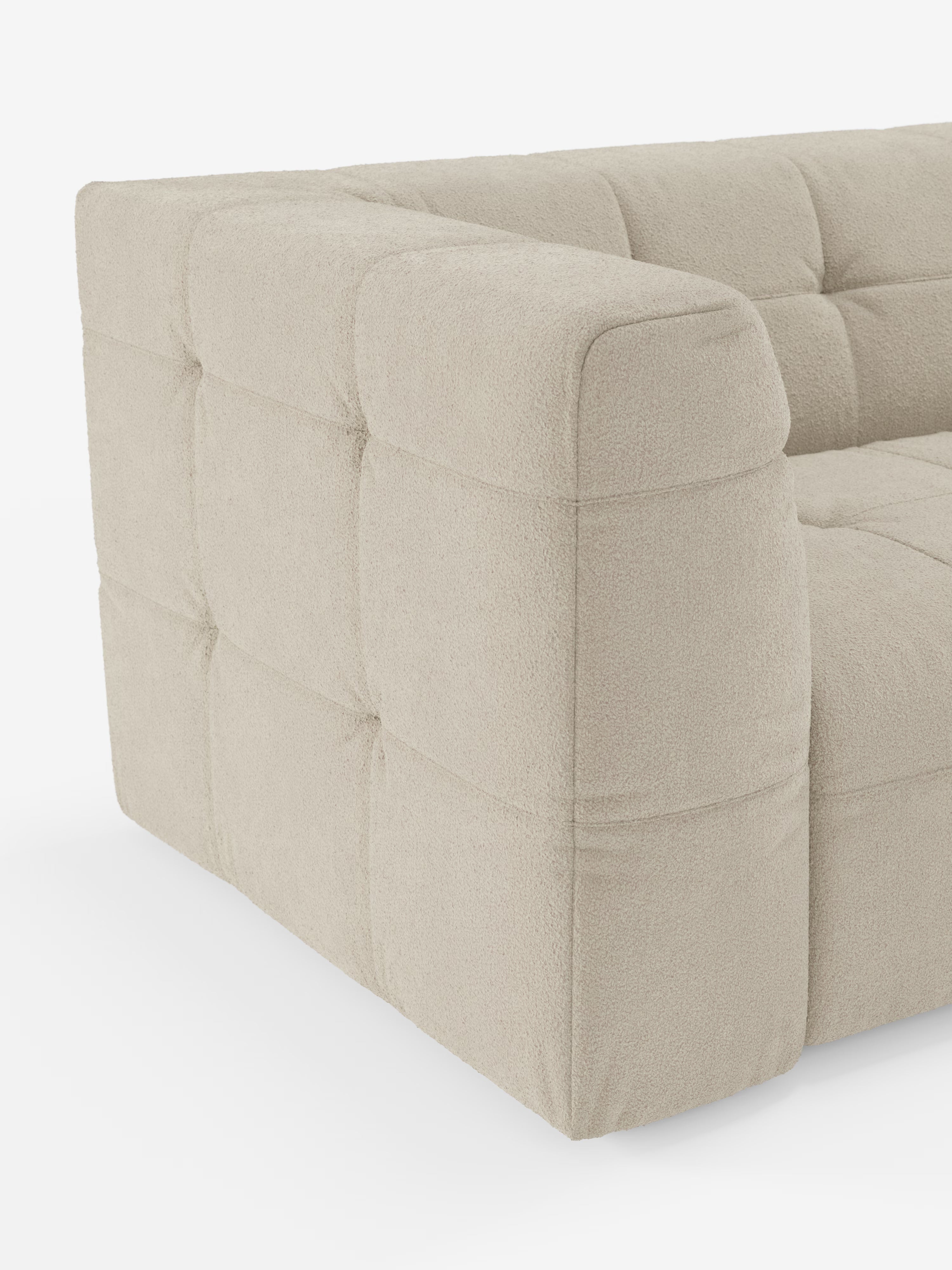 Un primo piano del divano modulare Mosaic a 3 e 4 posti in bouclé: imbottitura capitonné e design in tessuto antimacchia T21 di Divani.Store. Questo moderno divano componibile beige presenta un’elegante tappezzeria capitonné con motivo a quadrati, realizzata in morbido tessuto bouclé dalla trama ricca. L'immagine mette in risalto il bracciolo sinistro e parte della seduta, il tutto su uno sfondo bianco a tinta unita.