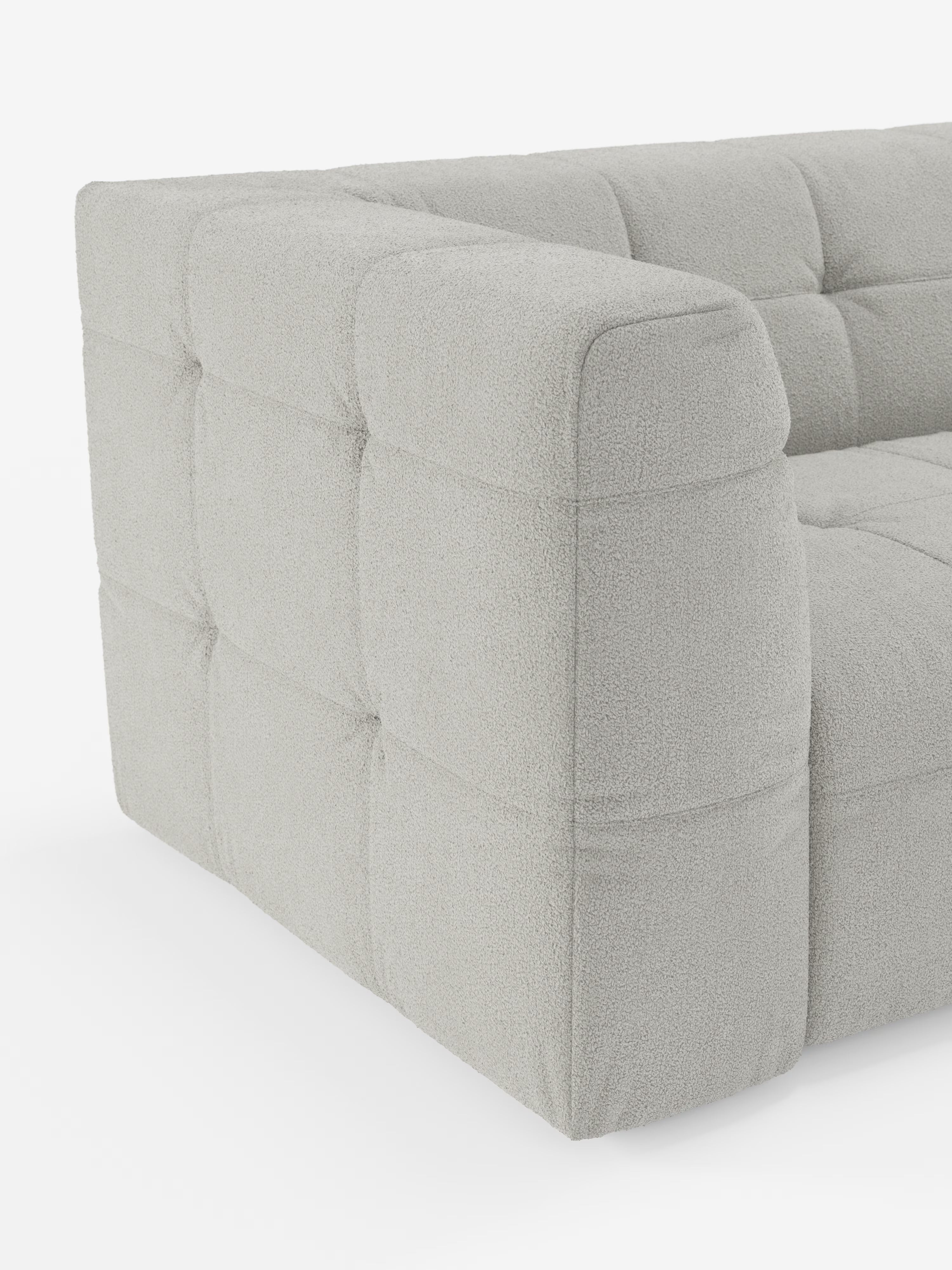 Un primo piano del divano modulare Mosaic a 3 e 4 posti in bouclé: capitonné e design in tessuto antimacchia T21 di Divani.Store, che mette in risalto il suo moderno rivestimento grigio chiaro con una finitura bouclé morbida e testurizzata. Il design è impreziosito da una profonda trapuntatura a quadrati sui braccioli, sui fianchi e sulla seduta, che conferisce a questo divano modulare un aspetto morbido e imbottito. Il tutto su uno sfondo bianco a tinta unita.