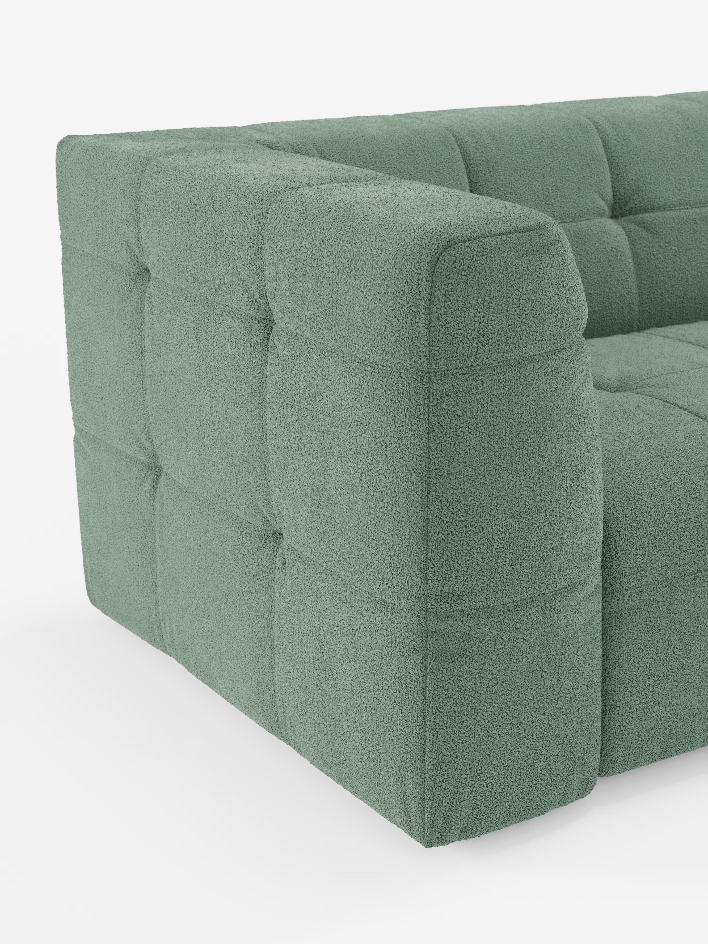 Un primo piano del divano componibile a 3 posti “Mosaic Divano” in bouclé di Divani.Store mette in risalto il suo tessuto T21 moderno, ecologico e antimacchia, caratterizzato da un raffinato motivo capitonné. Il divano presenta braccioli e schienale squadrati con ampie sezioni rettangolari trapuntate, disposte a intervalli regolari. Lo sfondo bianco a tinta unita esalta lo stile moderno del divano e i dettagli intricati del suo tessuto testurizzato.