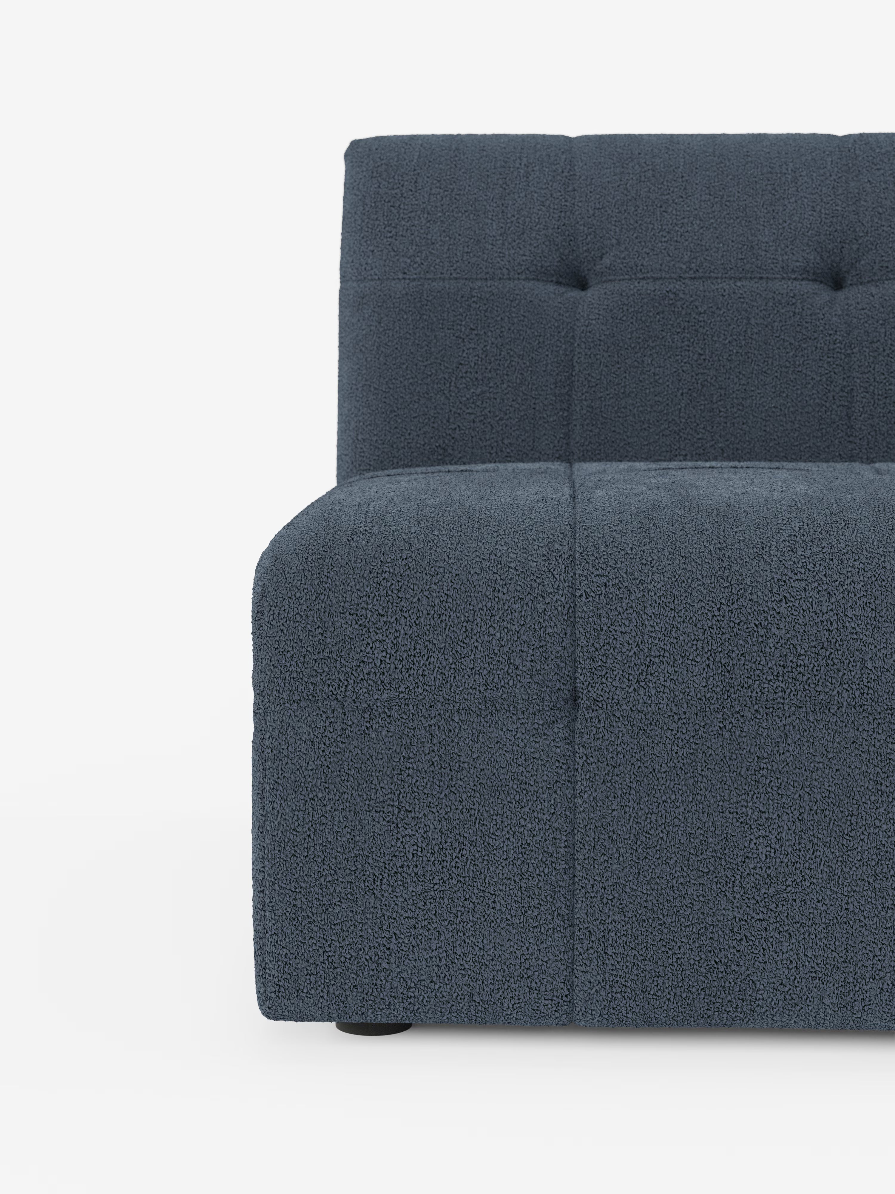 Un primo piano della poltrona Mosaic modulo da 77 cm di Divani.Store ne mette in risalto la forma moderna e senza braccioli, rivestita in tessuto bouclé blu scuro antimacchia con una caratteristica griglia capitonné composta da grandi quadrati morbidi e sottili dettagli trapuntati. Ispirata al design classico delle poltrone, questa seduta dalle linee minimaliste e squadrate poggia su piccole gambe nere su uno sfondo bianco a tinta unita.