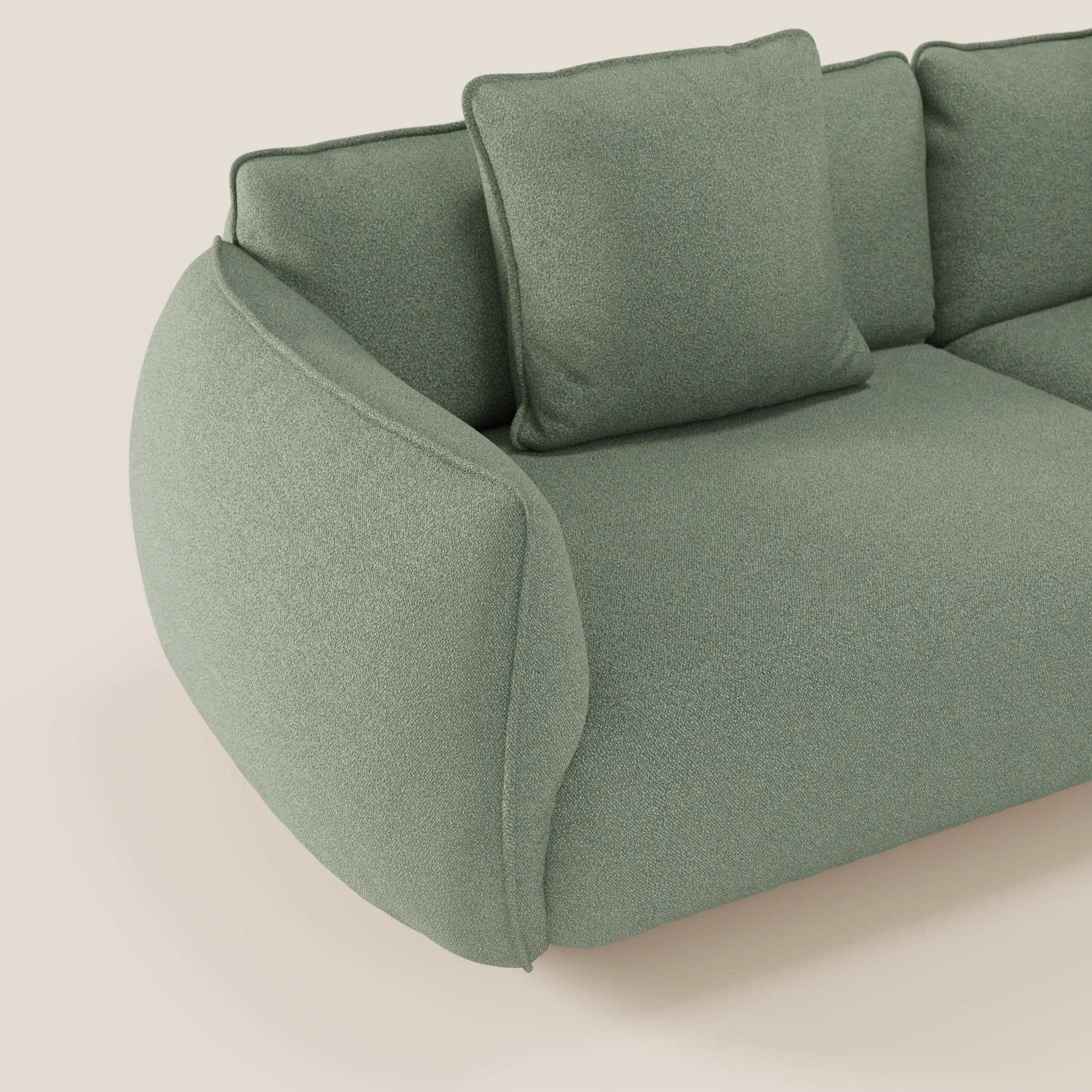 Il divano Nimbus angolare con penisola componibile di Divani.Store in morbido tessuto T33 antimacchia effetto cotone è presentato in verde chiaro con braccioli arrotondati, schienale morbido e due cuscini coordinati su sfondo beige. È visibile solo una parte.
