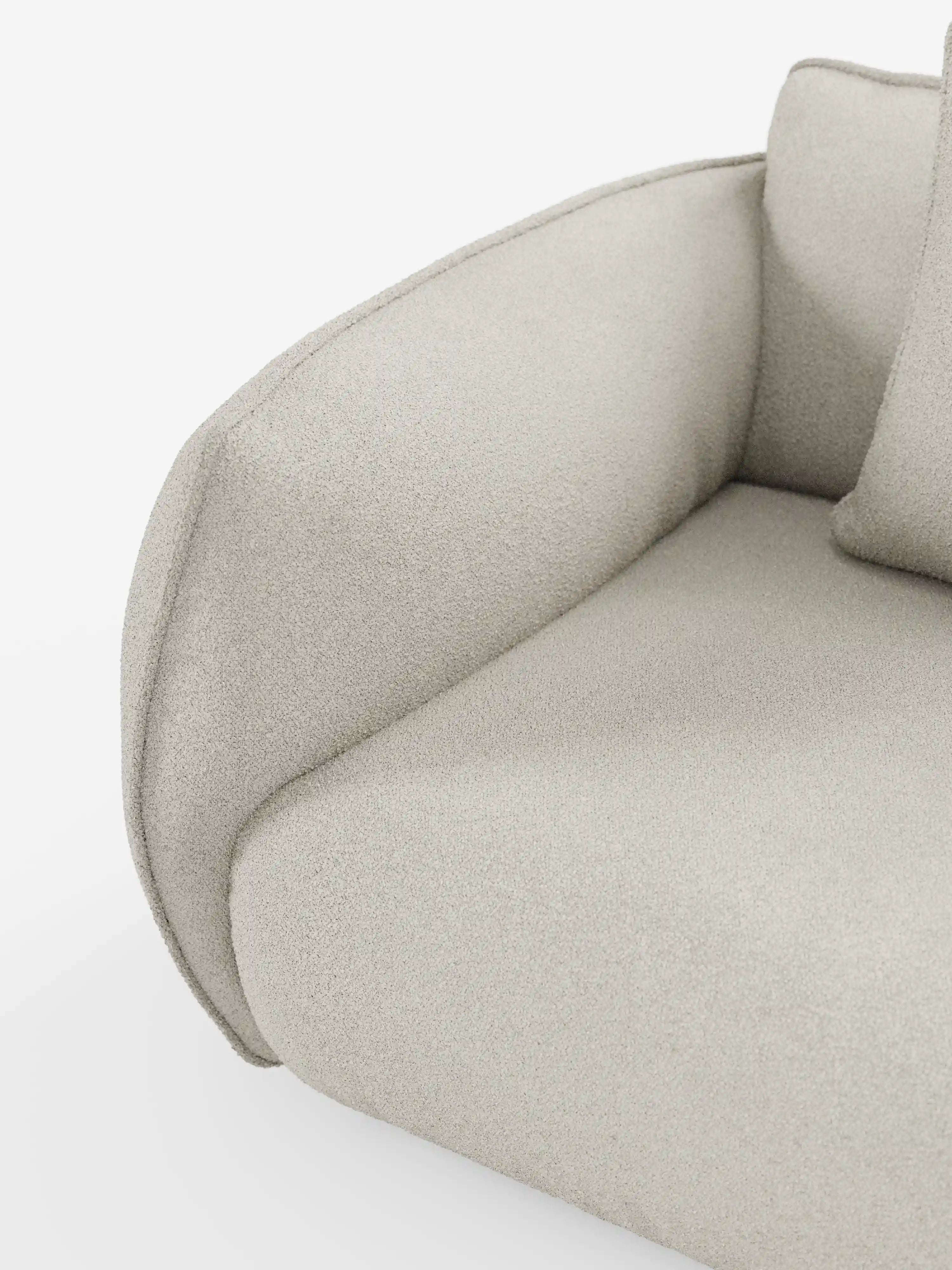 Primo piano di un moderno divano Nimbus a 3 posti, modulare e componibile, di Divani.Store, rivestito in tessuto T33 beige chiaro, testurizzato e smacchiabile, effetto cotone. I braccioli e lo schienale si snodano in curve morbide, conferendo al divano un aspetto soffice e arrotondato. Un cuscino coordinato è parzialmente visibile su uno sfondo bianco a tinta unita.