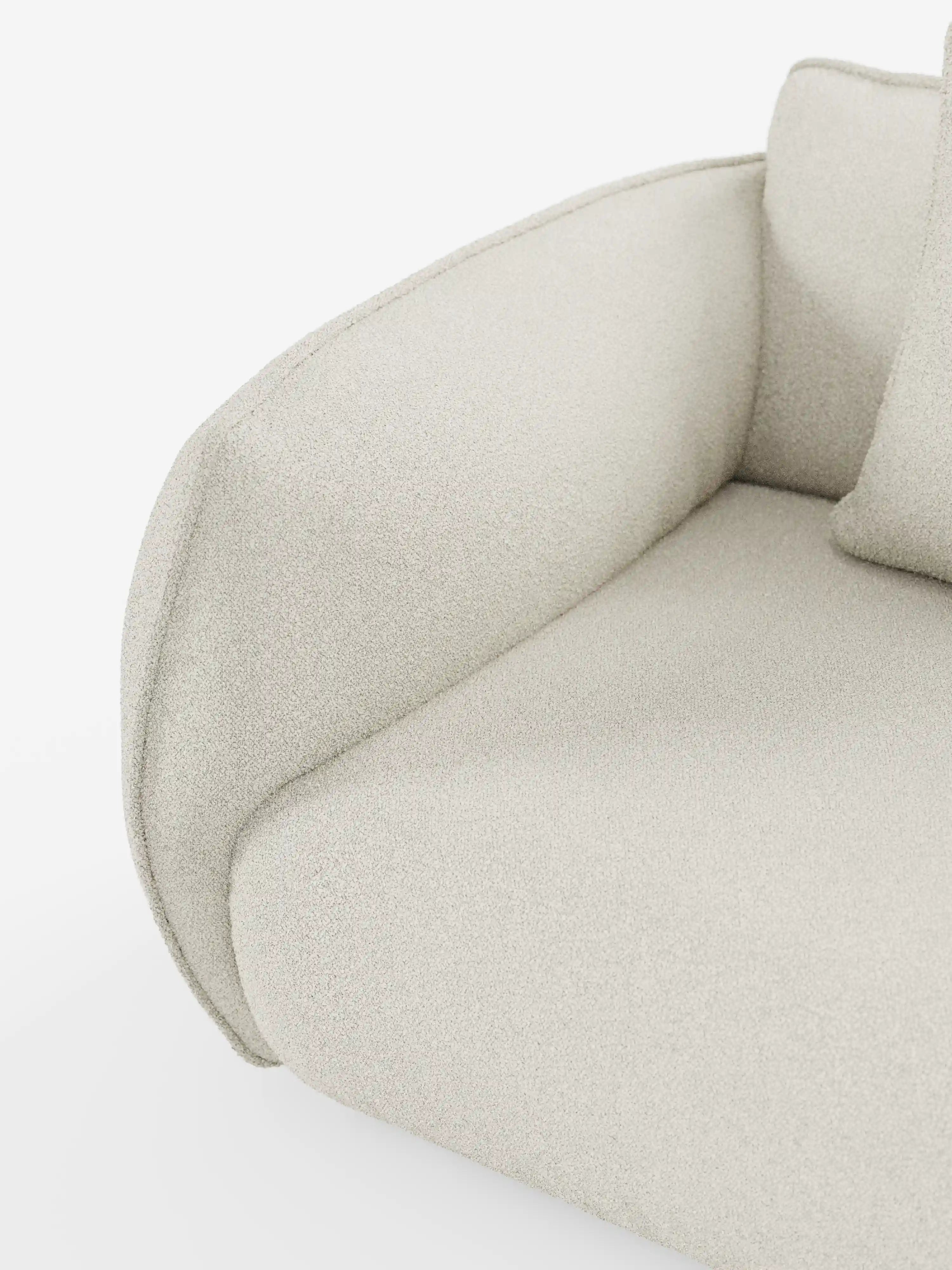 Primo piano del divano modulare e componibile a 3 posti Nimbus da 250 cm di Divani.Store, rivestito in tessuto T33 beige chiaro, testurizzato, smacchiabile, effetto cotone. Il bracciolo delicatamente ricurvo e un cuscino coordinato appoggiato allo schienale ne sottolineano il design moderno. Questo divano modulare è esposto su uno sfondo bianco e liscio.